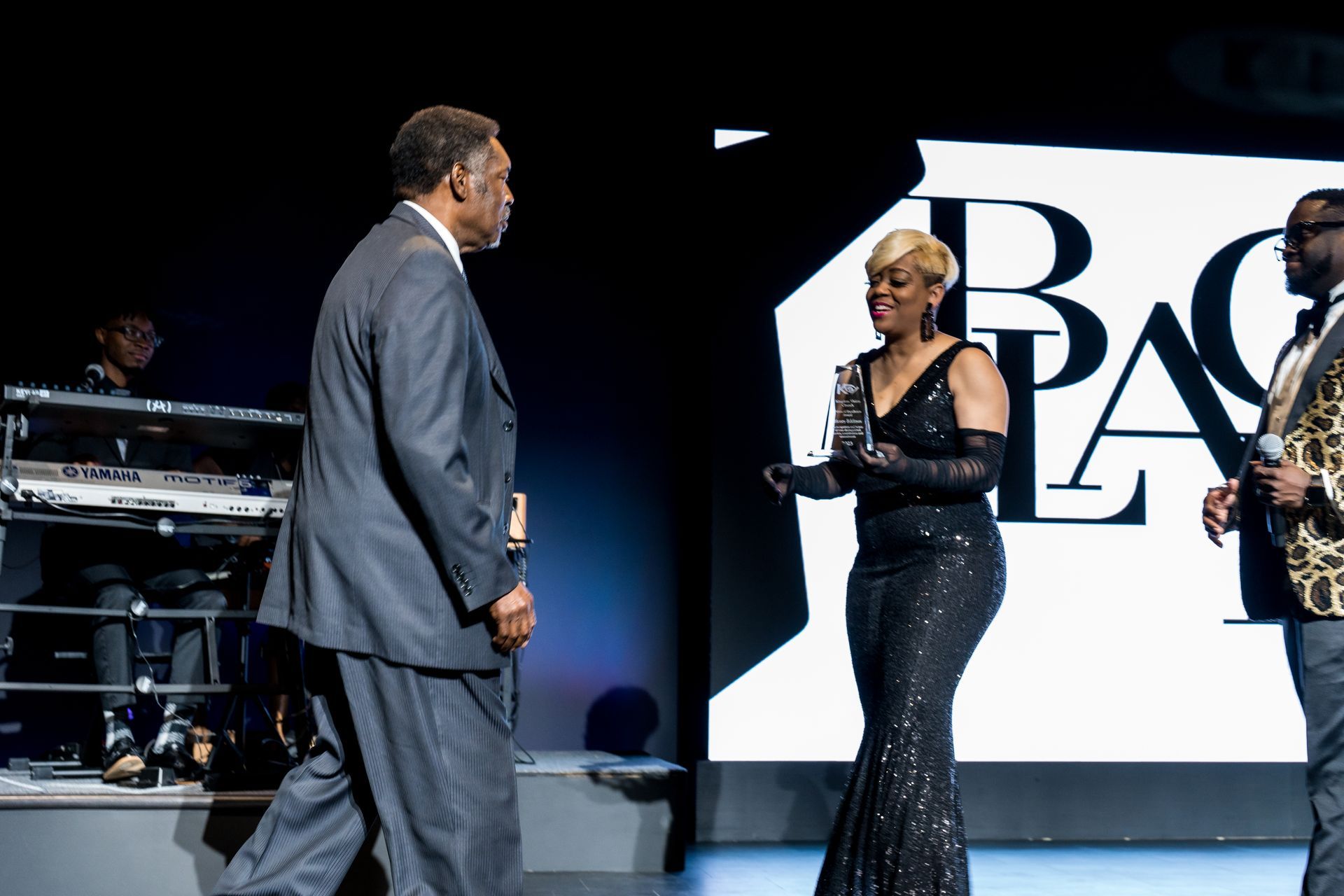 A man in a suit stands next to a woman in a black dress holding a trophy