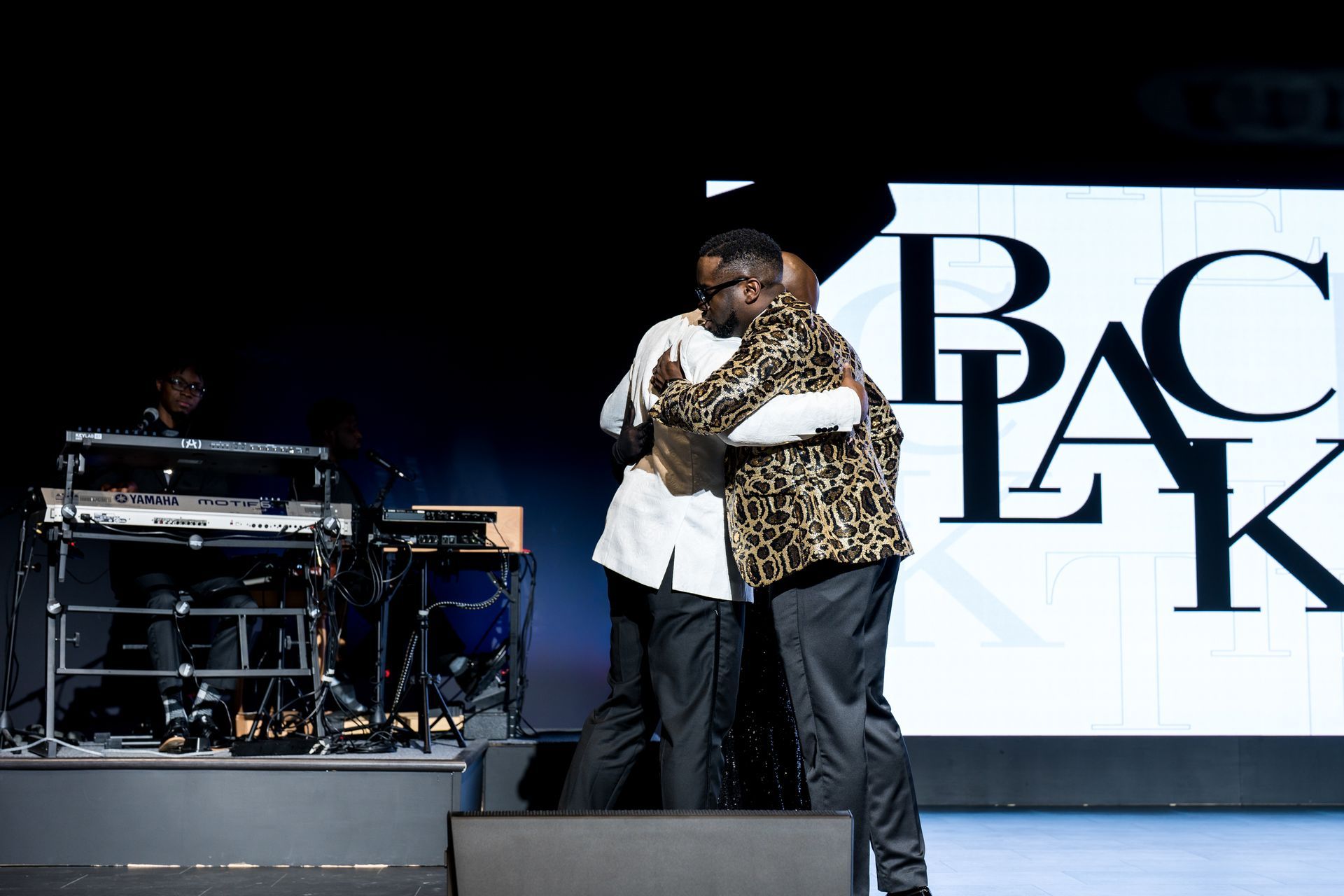 A group of men are hugging on a stage in front of a pac logo