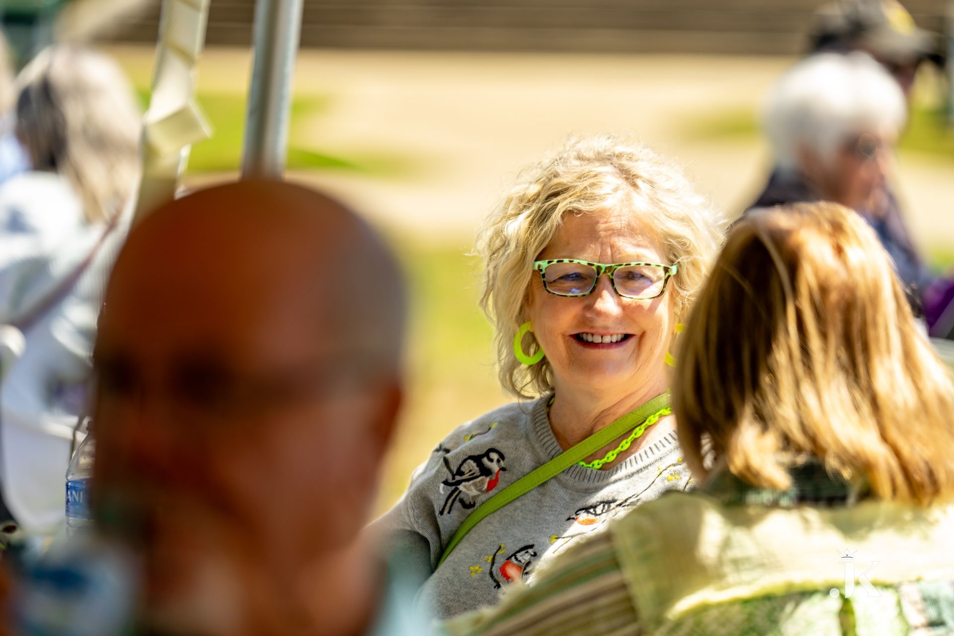 A woman wearing glasses is smiling while talking to a group of people.