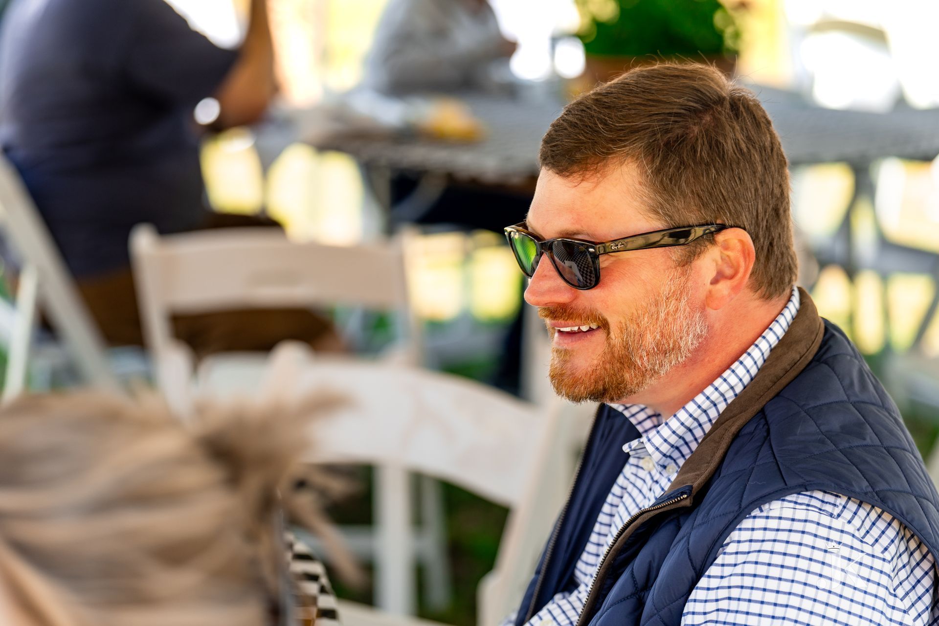 A man wearing sunglasses and a vest is sitting in a chair.