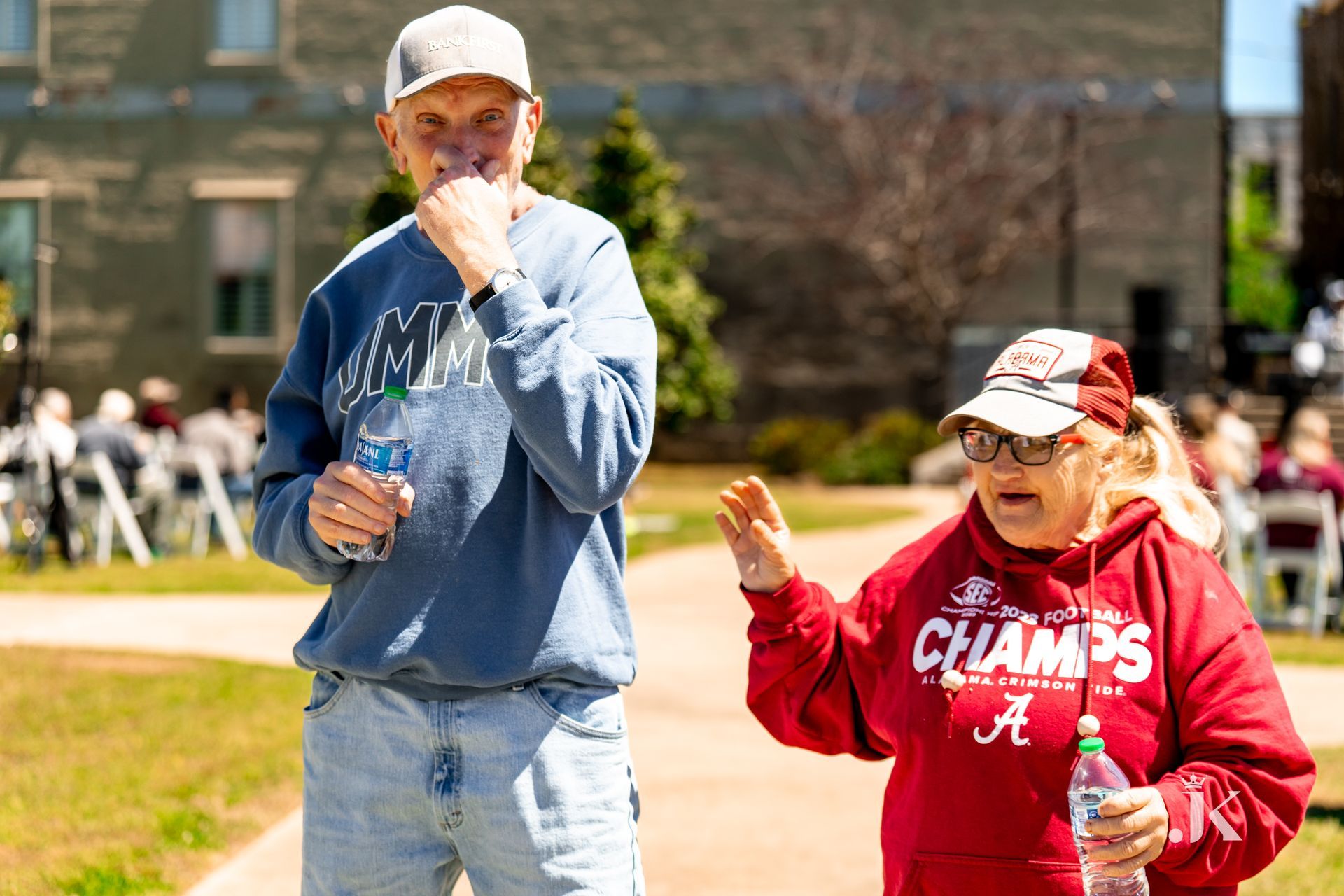 A man and a woman are drinking water from bottles while walking down a sidewalk.