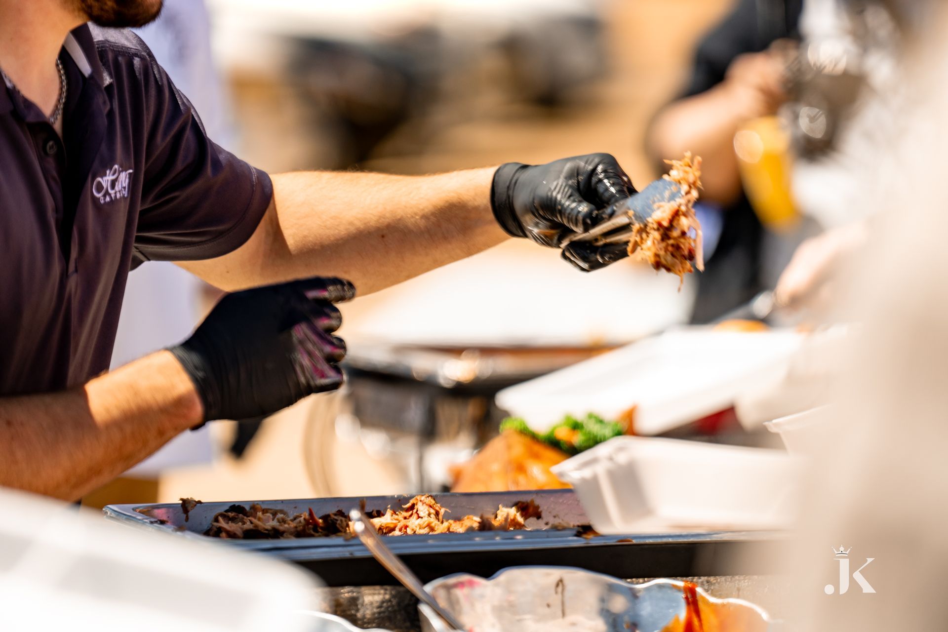 A man wearing black gloves is holding a piece of meat over a grill.