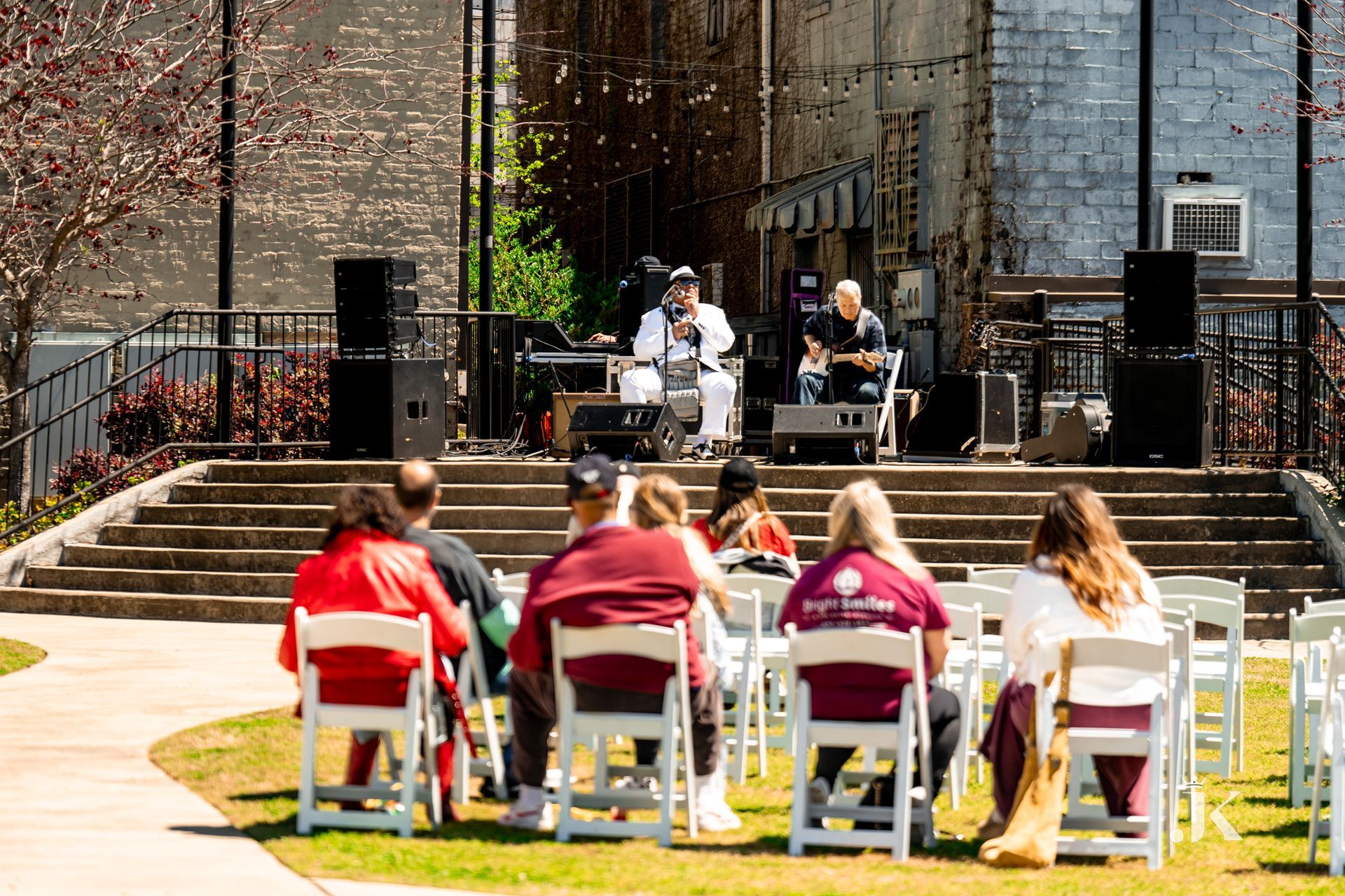 A group of people are sitting in white chairs in front of a stage.
