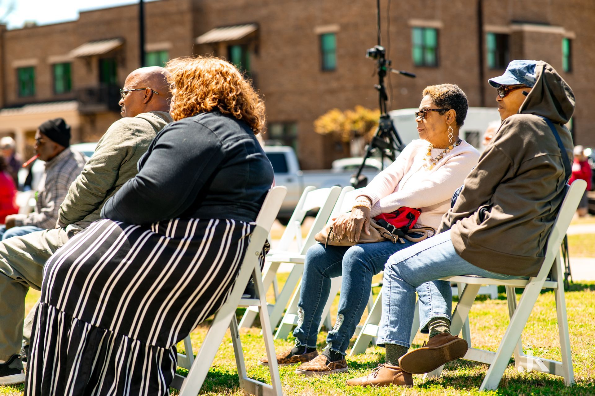 A group of people are sitting in white folding chairs in the grass.