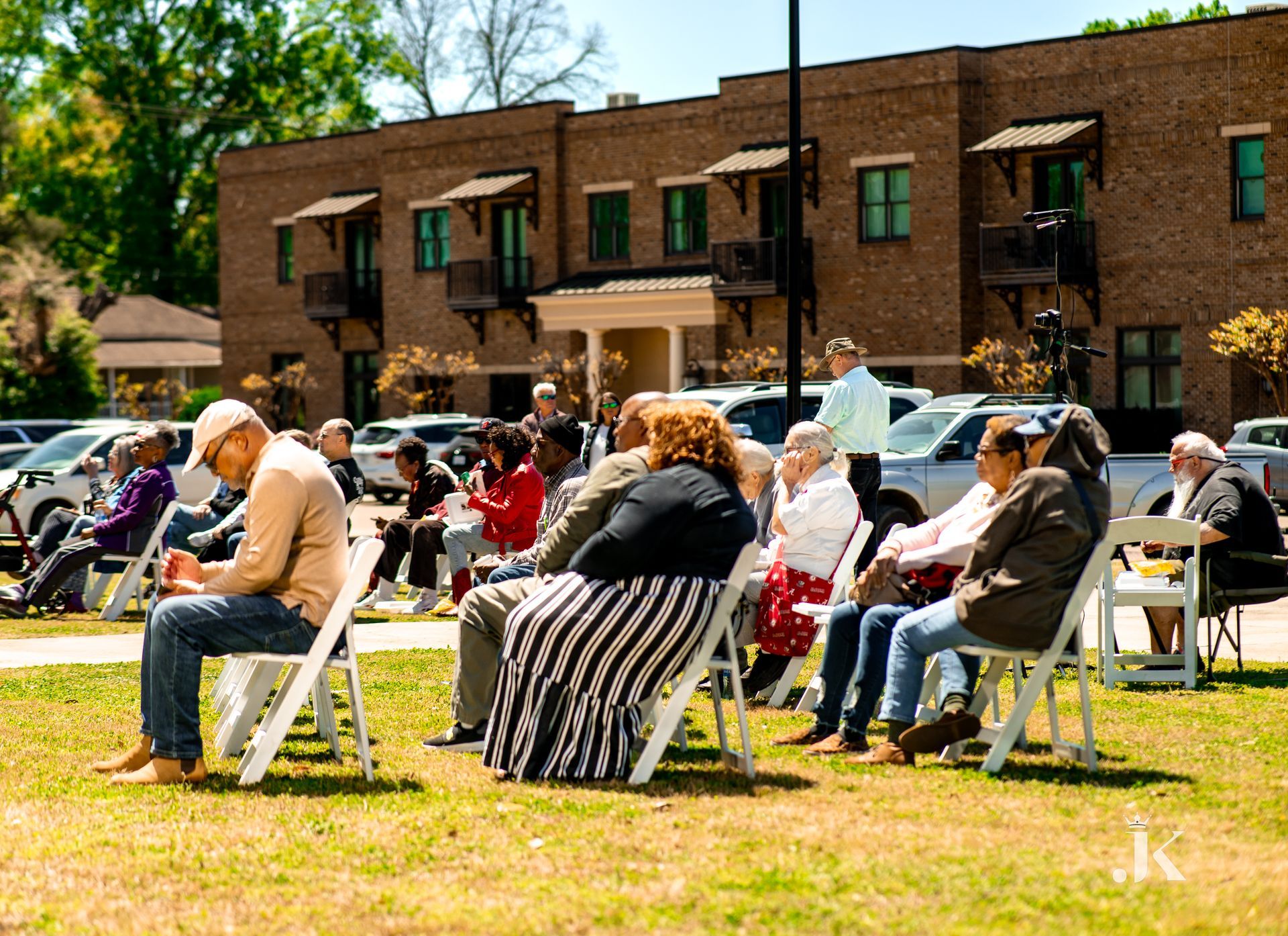 A group of people are sitting in chairs in front of a brick building.