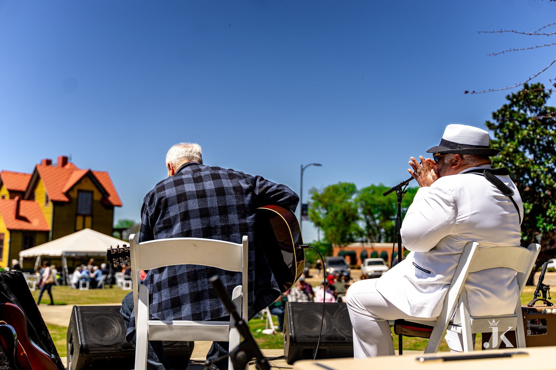 Two men are sitting in chairs playing guitars and singing into microphones.