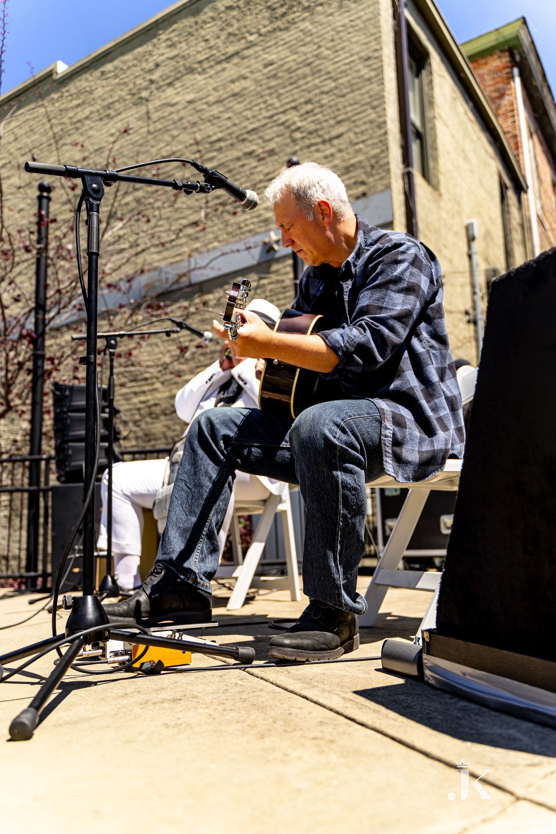 A man is sitting on a chair playing a guitar in front of a microphone.