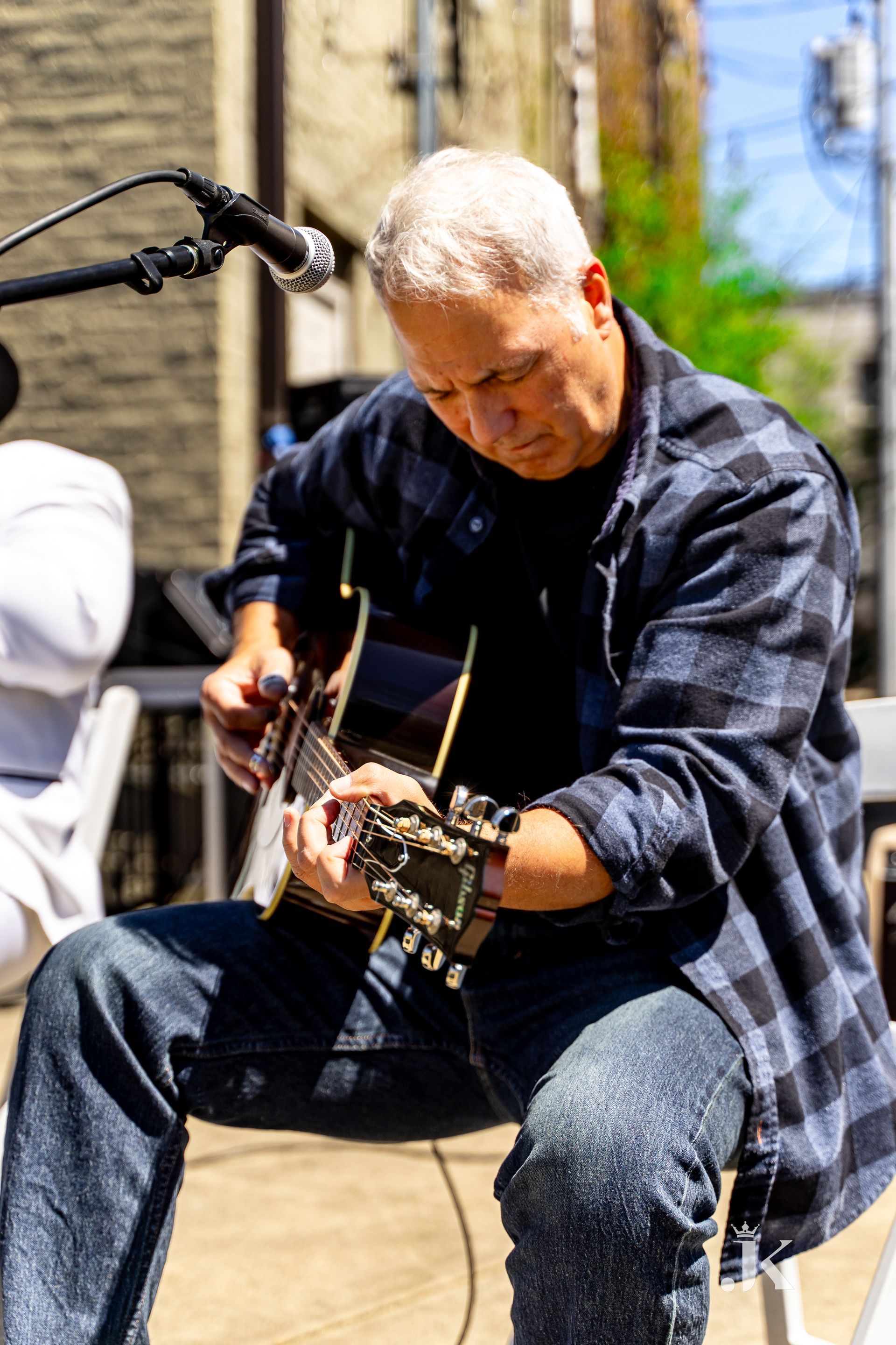 A man is sitting on a chair playing an acoustic guitar in front of a microphone.