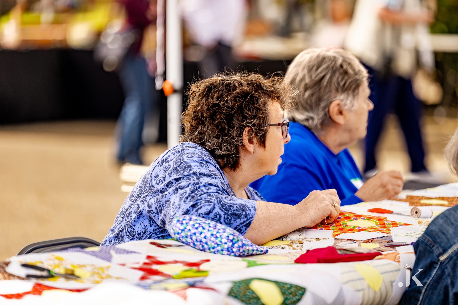A group of older women are sitting at a table making quilts.