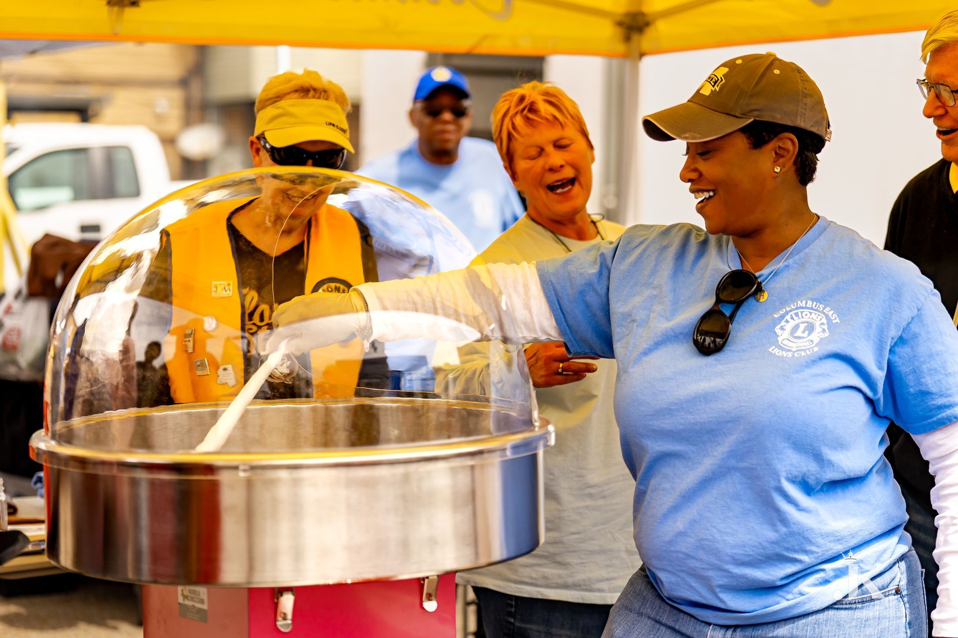 A woman in a blue shirt is standing in front of a cotton candy machine.