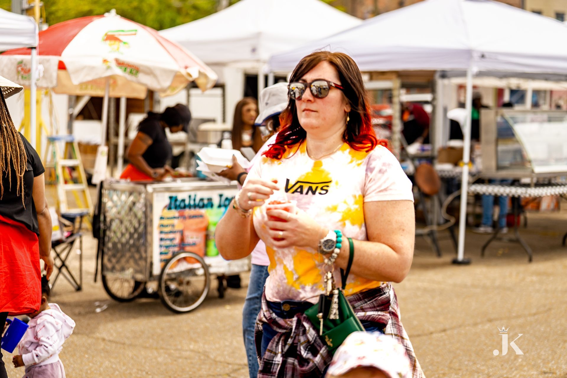 A woman wearing a vans shirt is standing in front of an ice cream cart.
