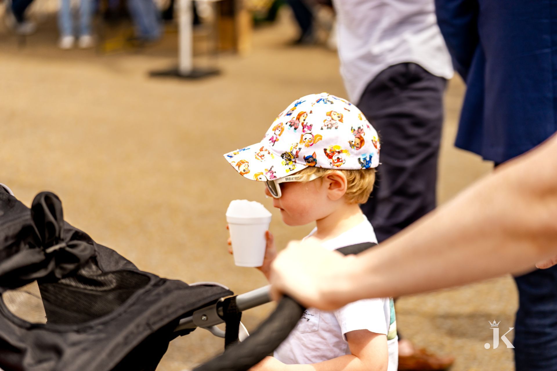 A little boy is sitting in a stroller drinking from a cup.