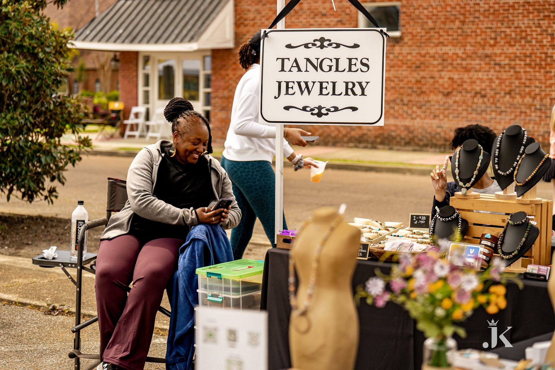 A woman is sitting in front of a sign that says tangles jewelry.