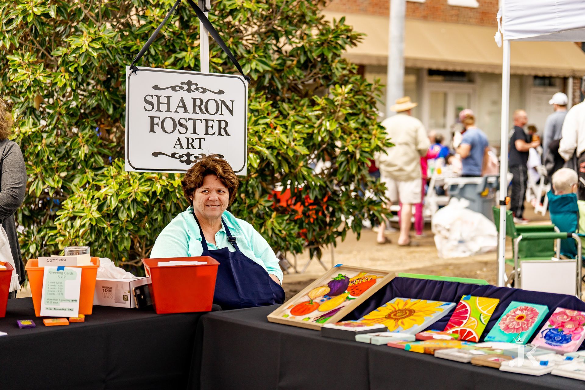 A woman is sitting at a table with a sign that says sharon foster art.
