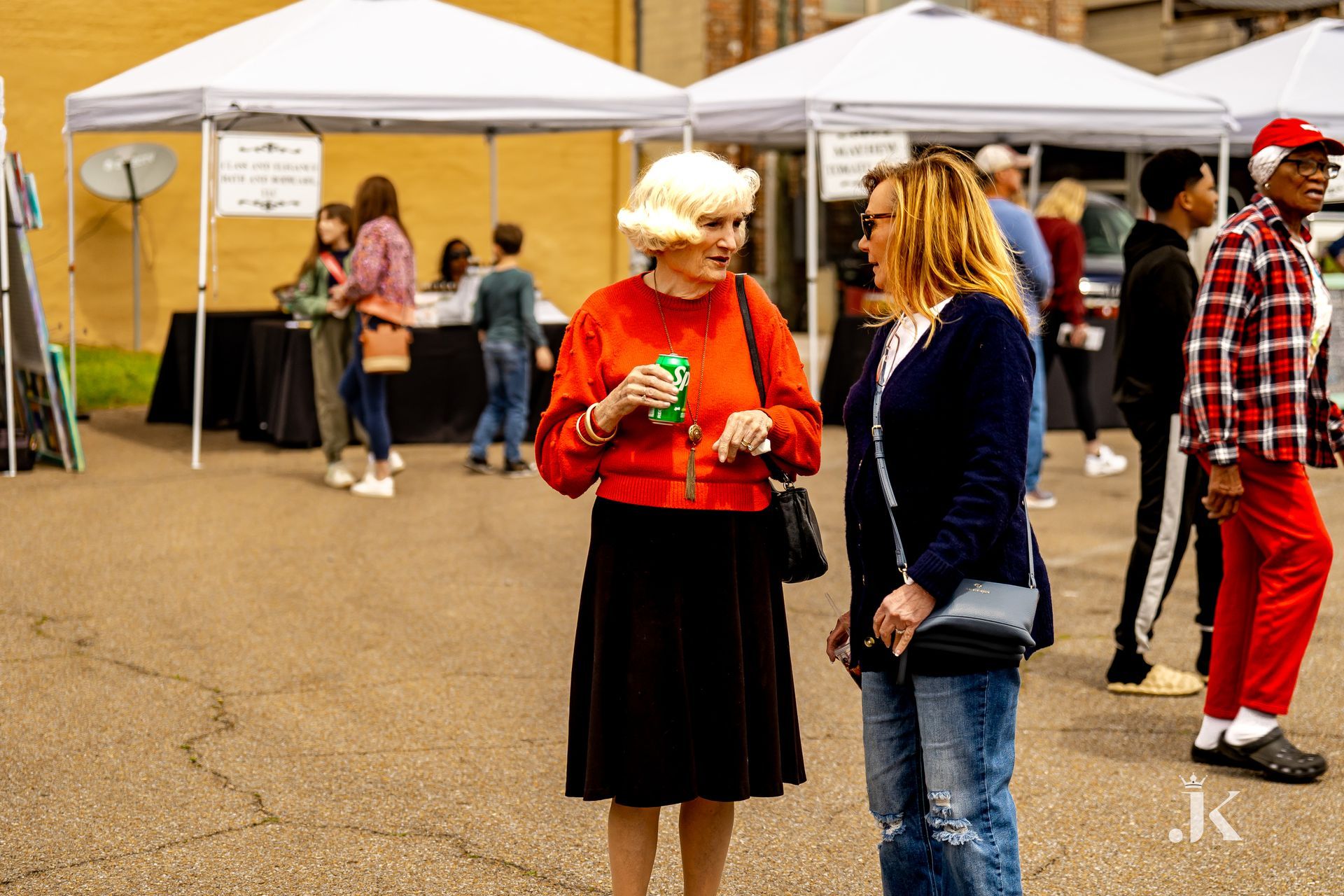 Two women are standing next to each other in a parking lot talking to each other.