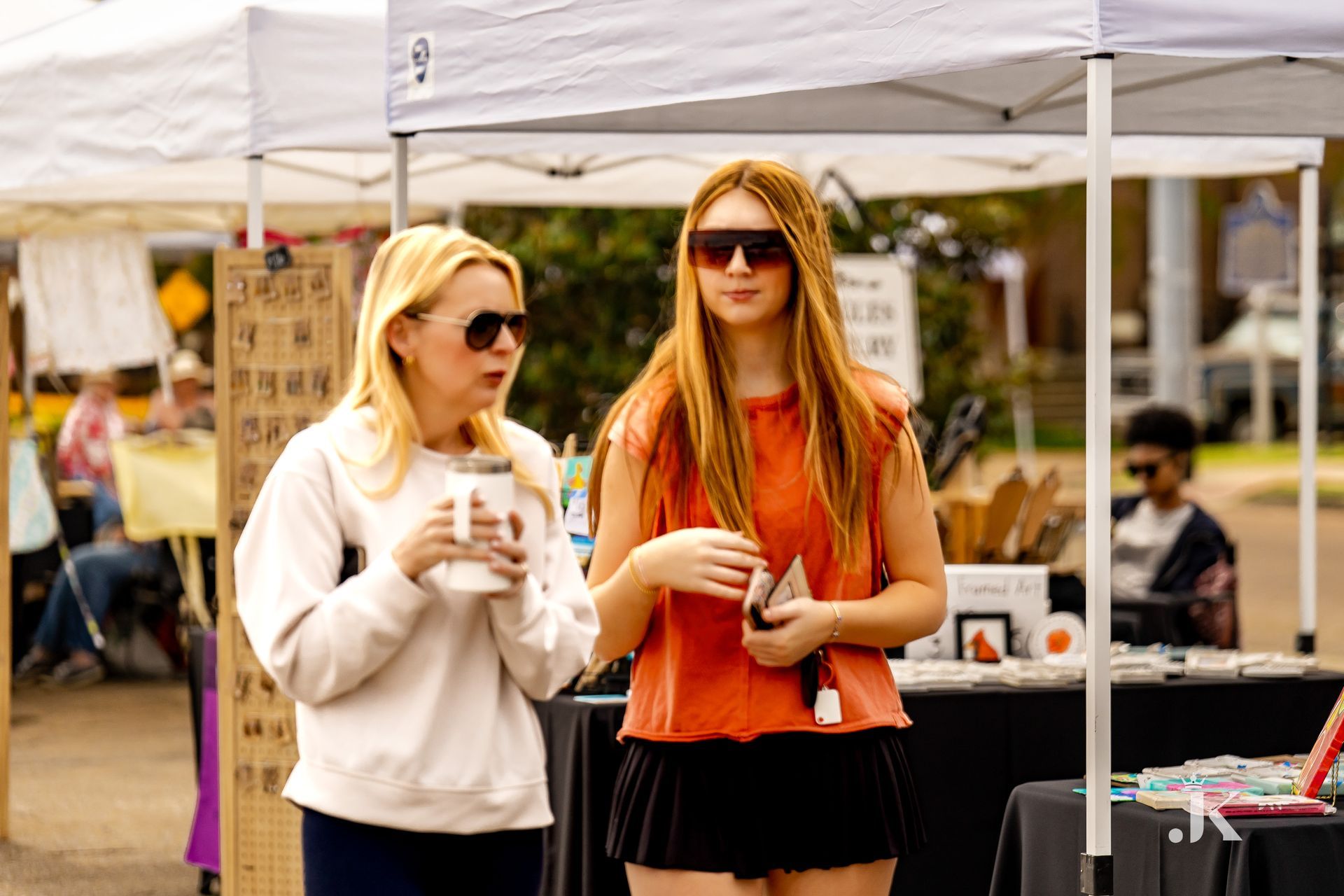 Two women are standing under a tent at a market.