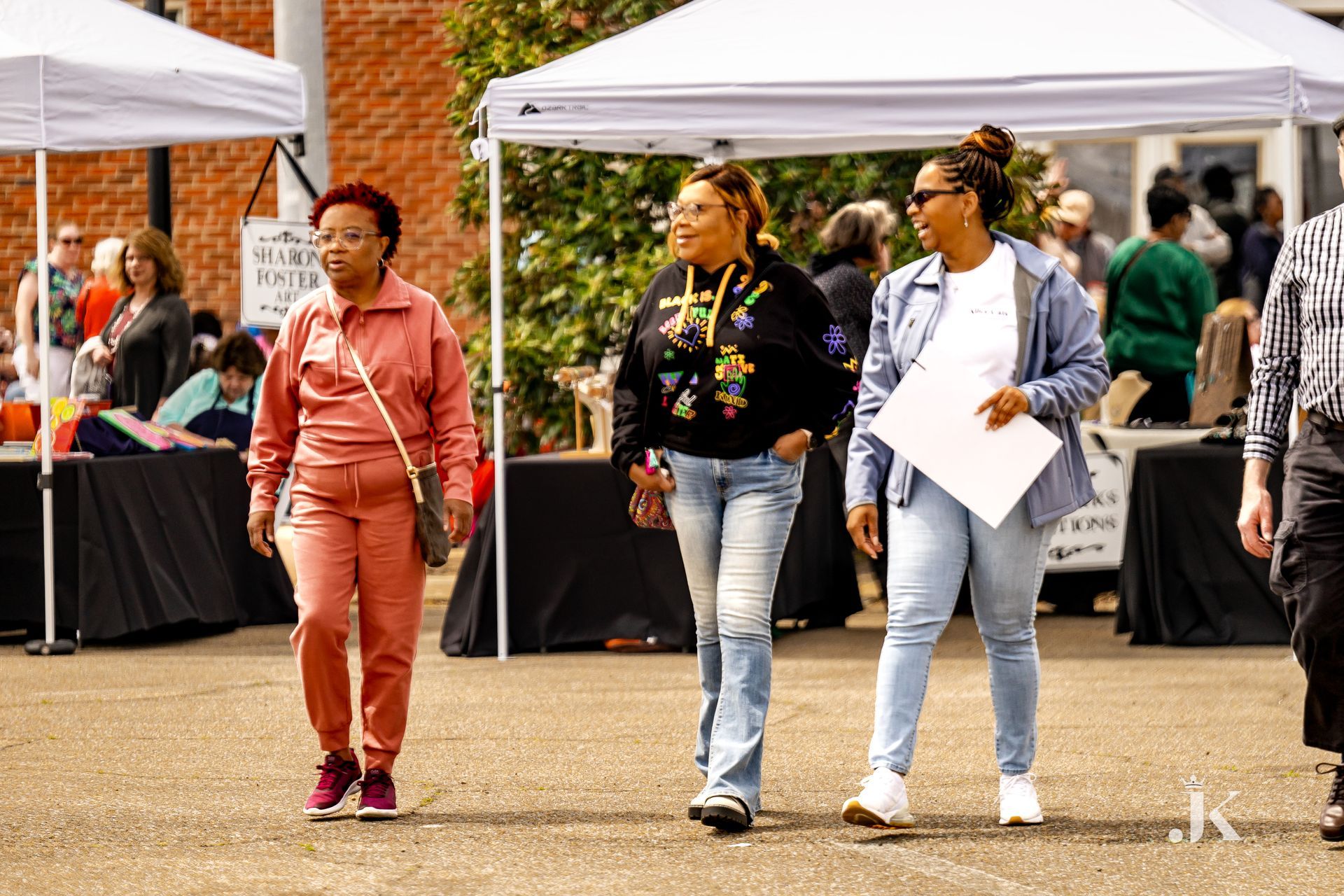 Three women are walking down a street in front of tents.