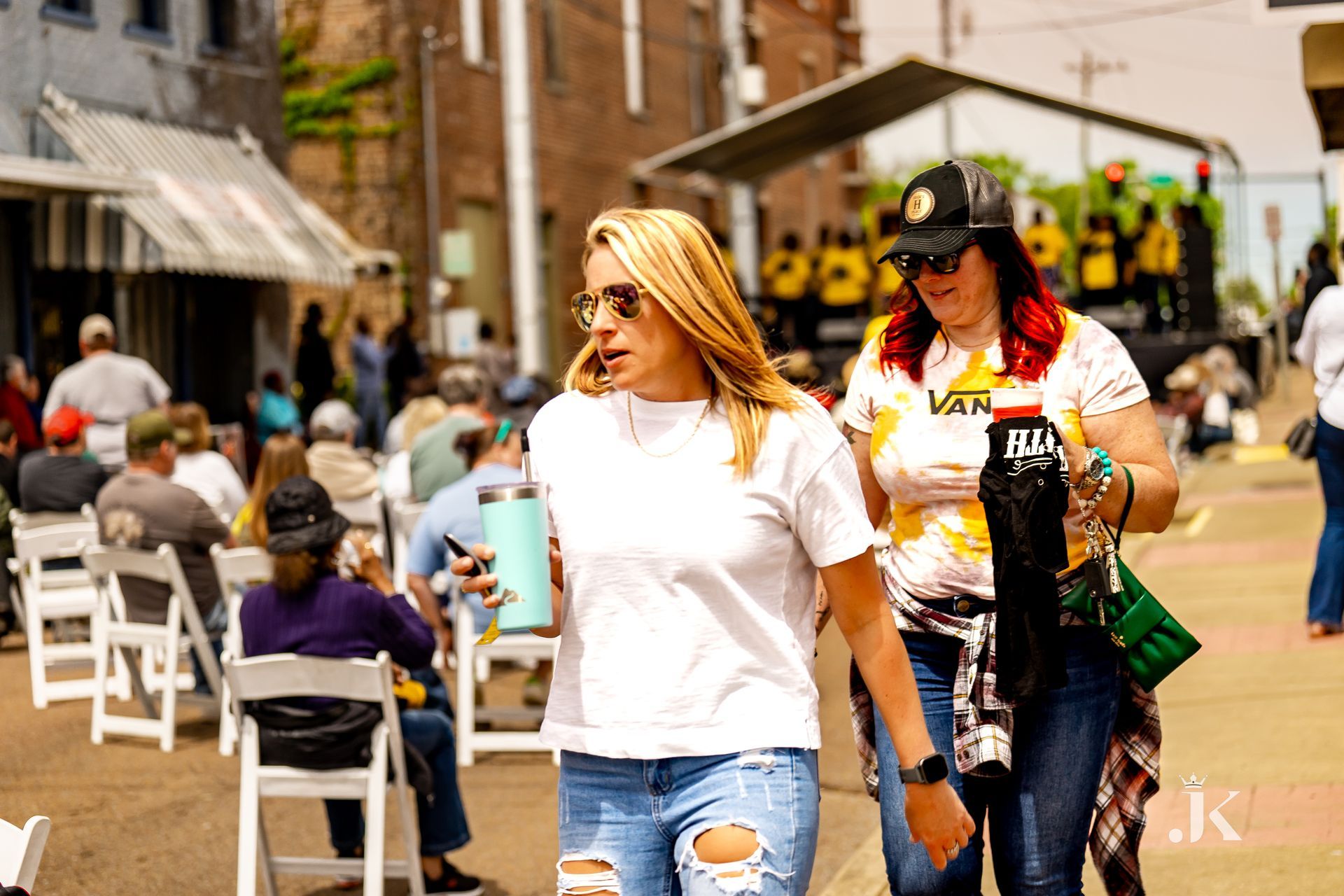 Two women are walking down a street in front of a crowd of people.