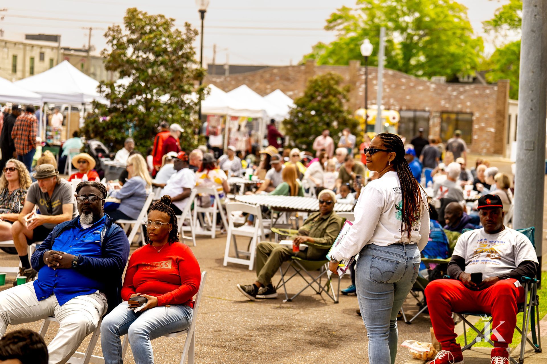 A woman is standing in front of a crowd of people sitting at tables and chairs.