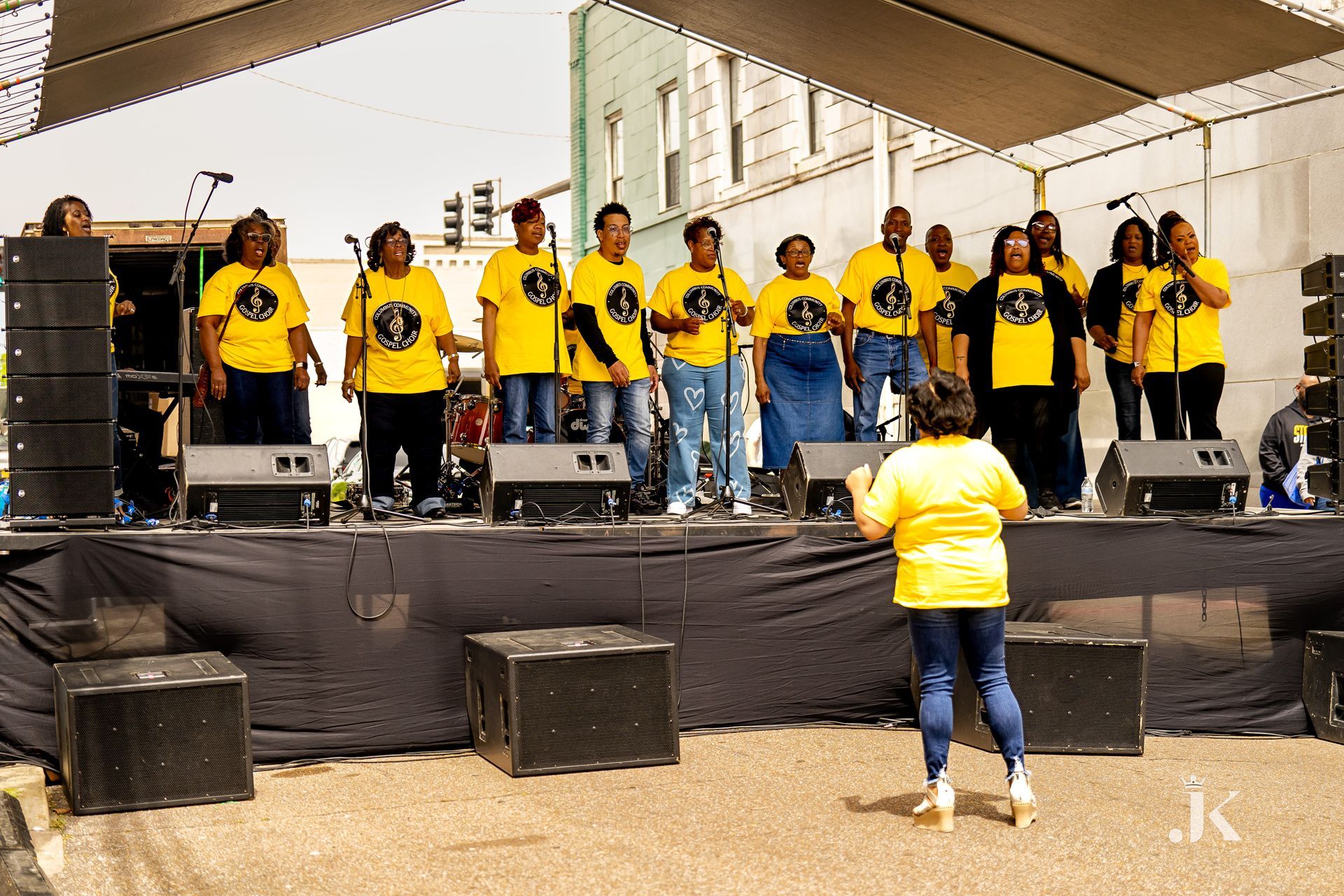 A group of people in yellow shirts are singing on a stage