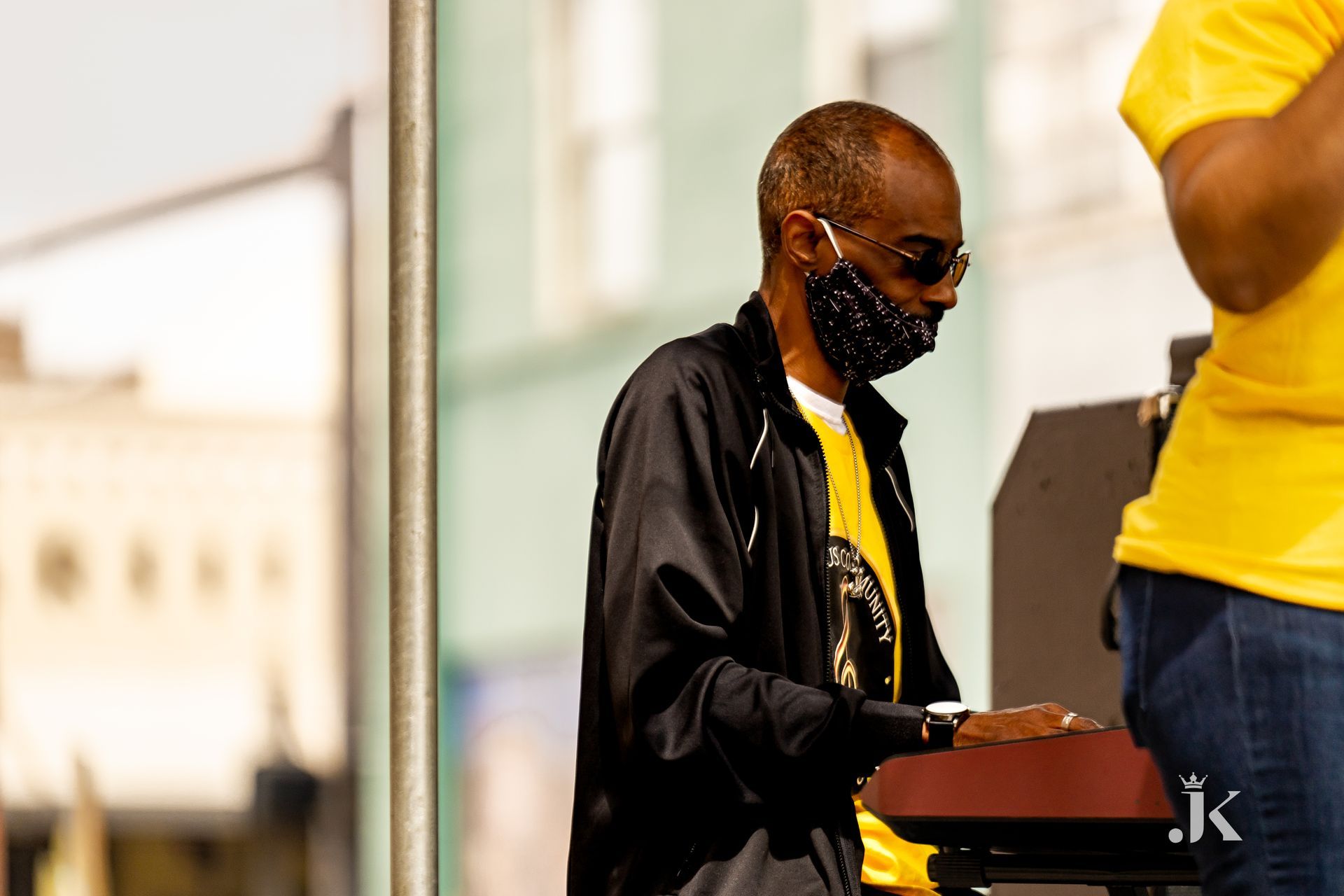 A man wearing a mask and sunglasses is standing next to another man.
