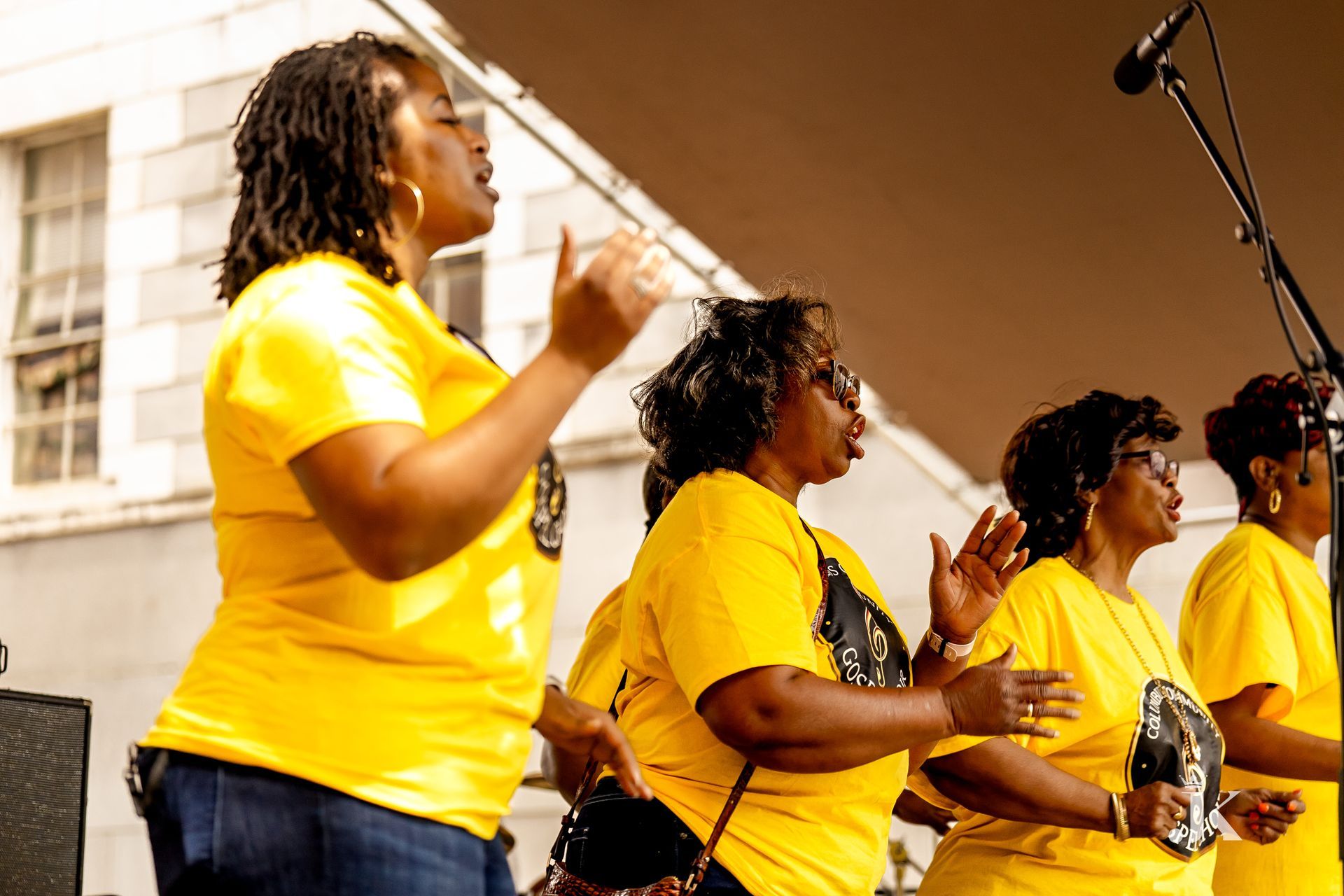 A group of women in yellow shirts are singing in front of a microphone