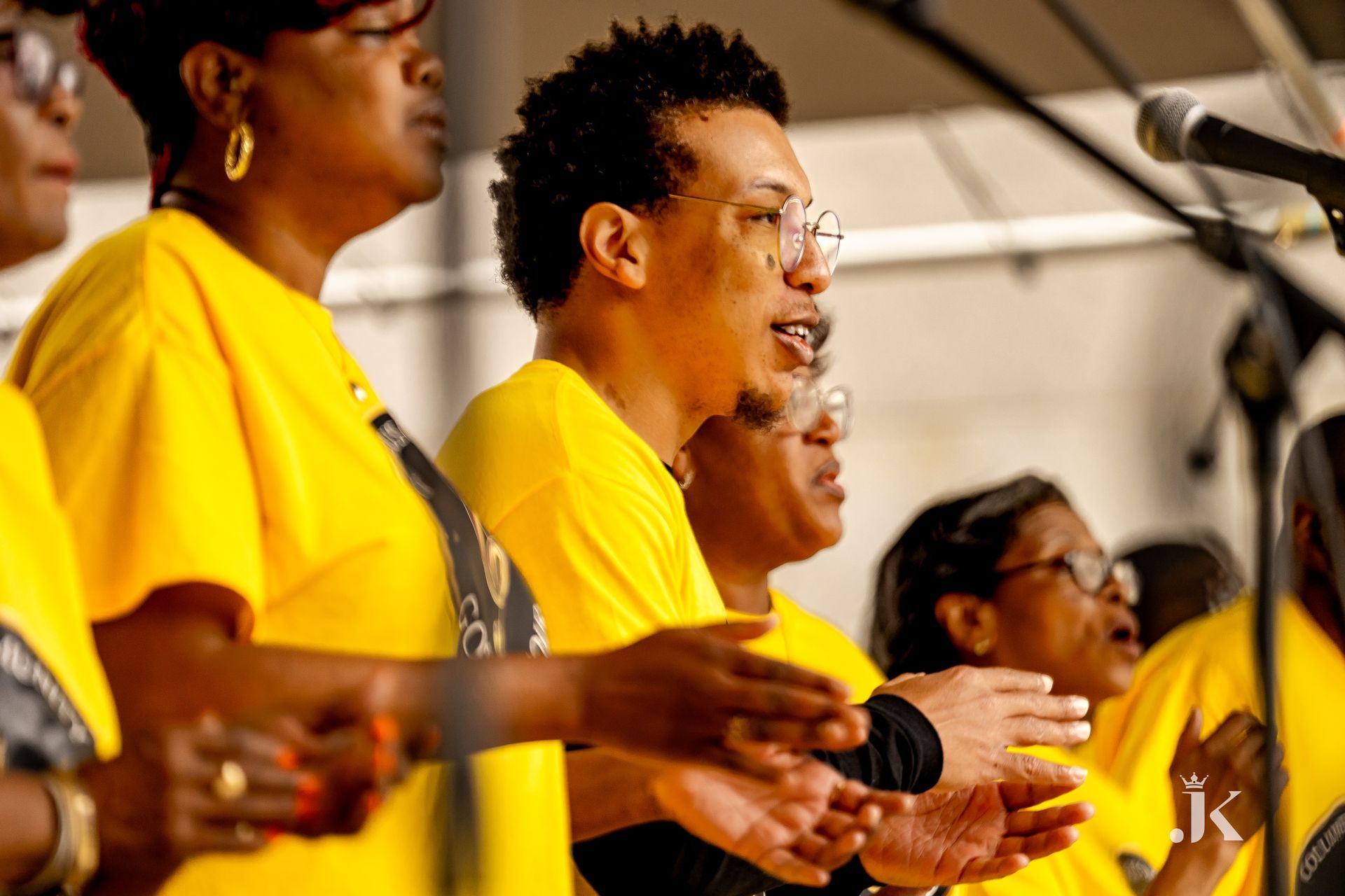 A group of people wearing yellow shirts are singing into microphones.
