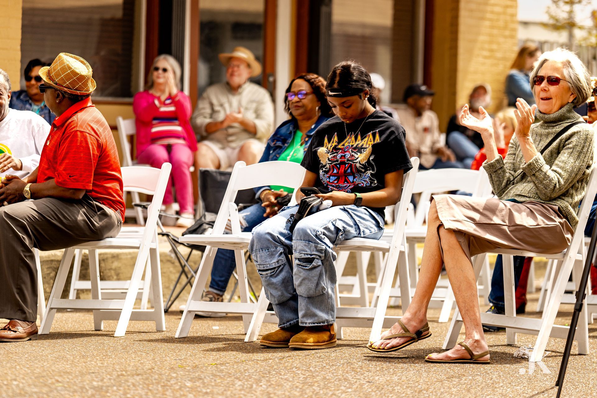 A group of people are sitting in white chairs outside.