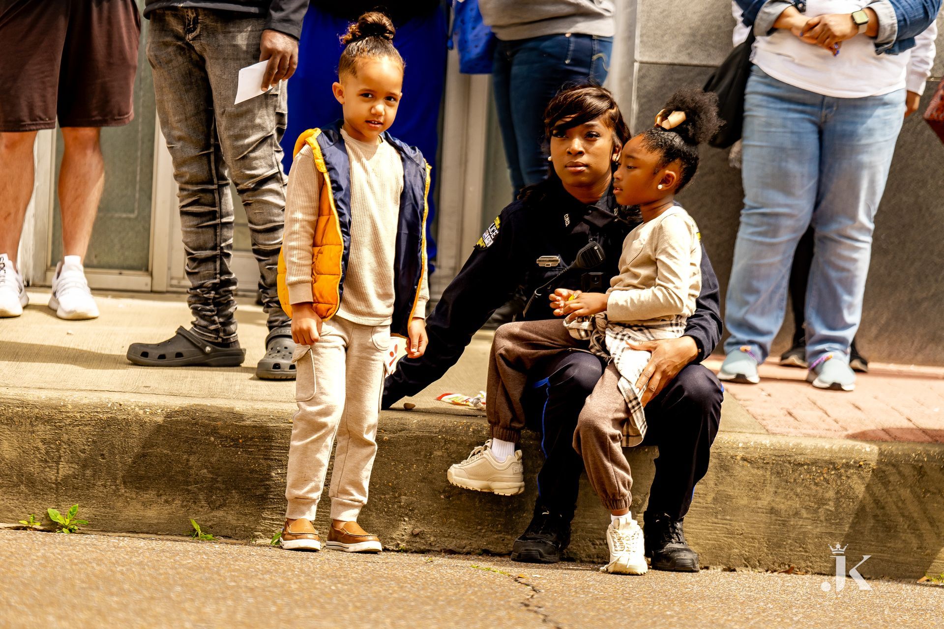 A woman is sitting on the sidewalk with two children.