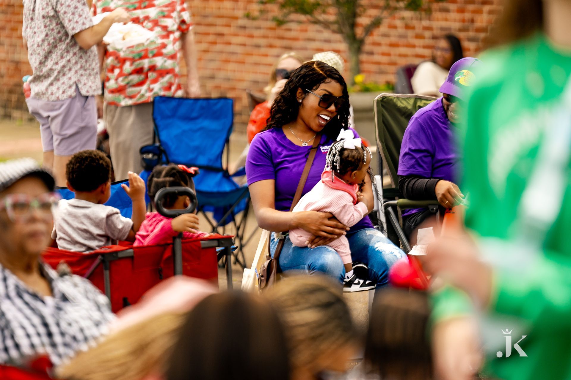 A woman is holding a baby while sitting in a crowd of people.