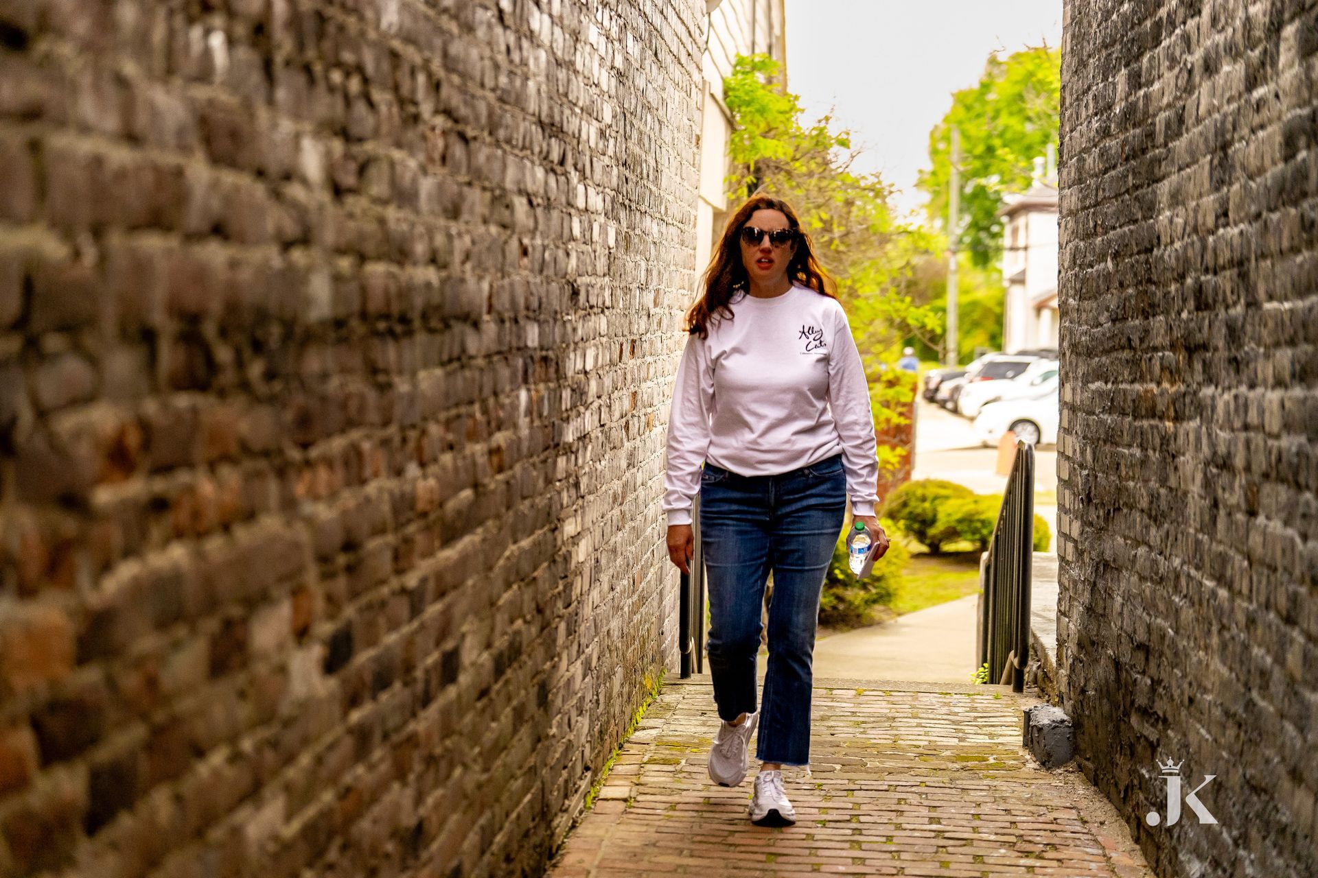 A woman is walking down a narrow alleyway next to a brick wall.