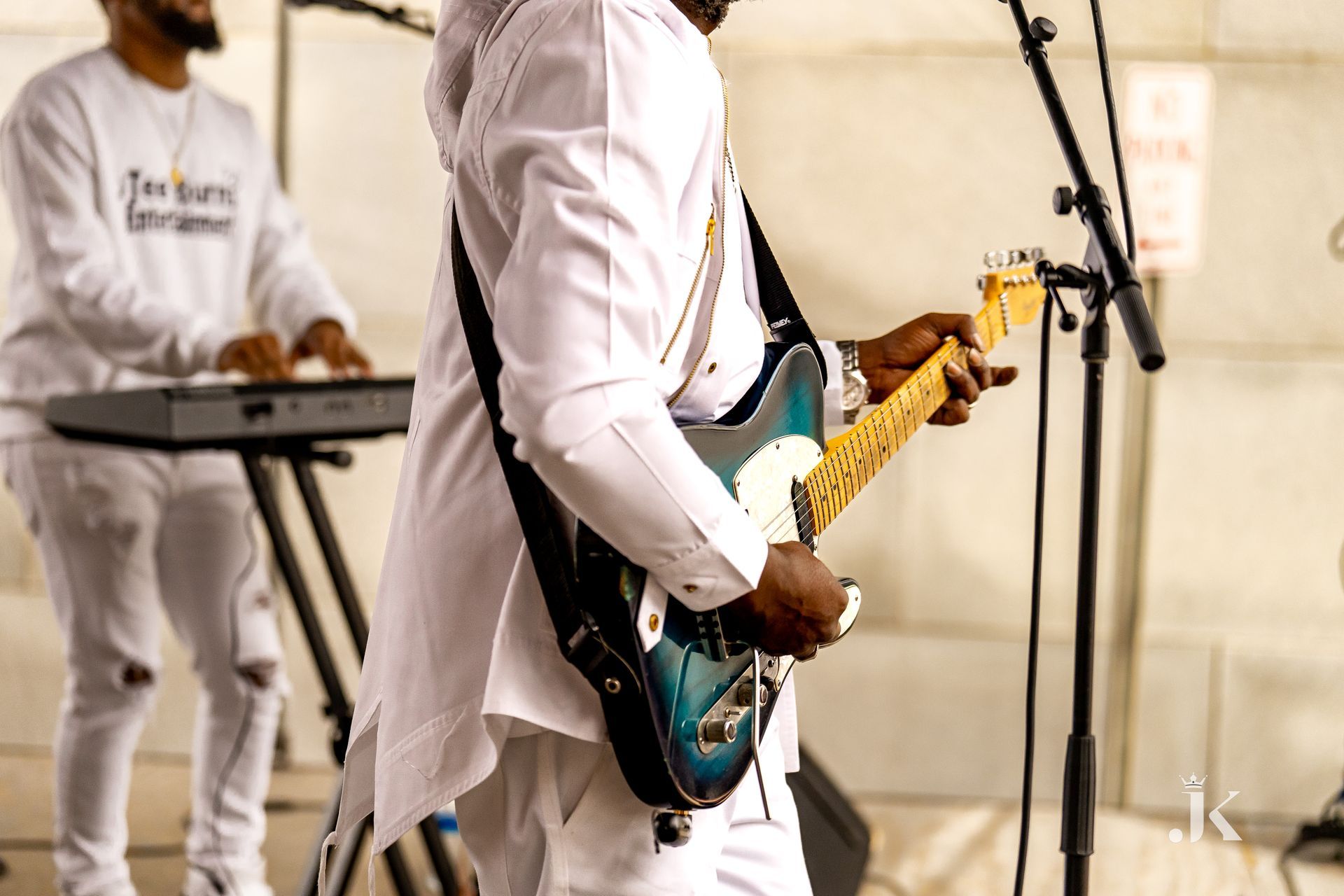 A man is playing a guitar in front of a microphone while another man plays a keyboard.