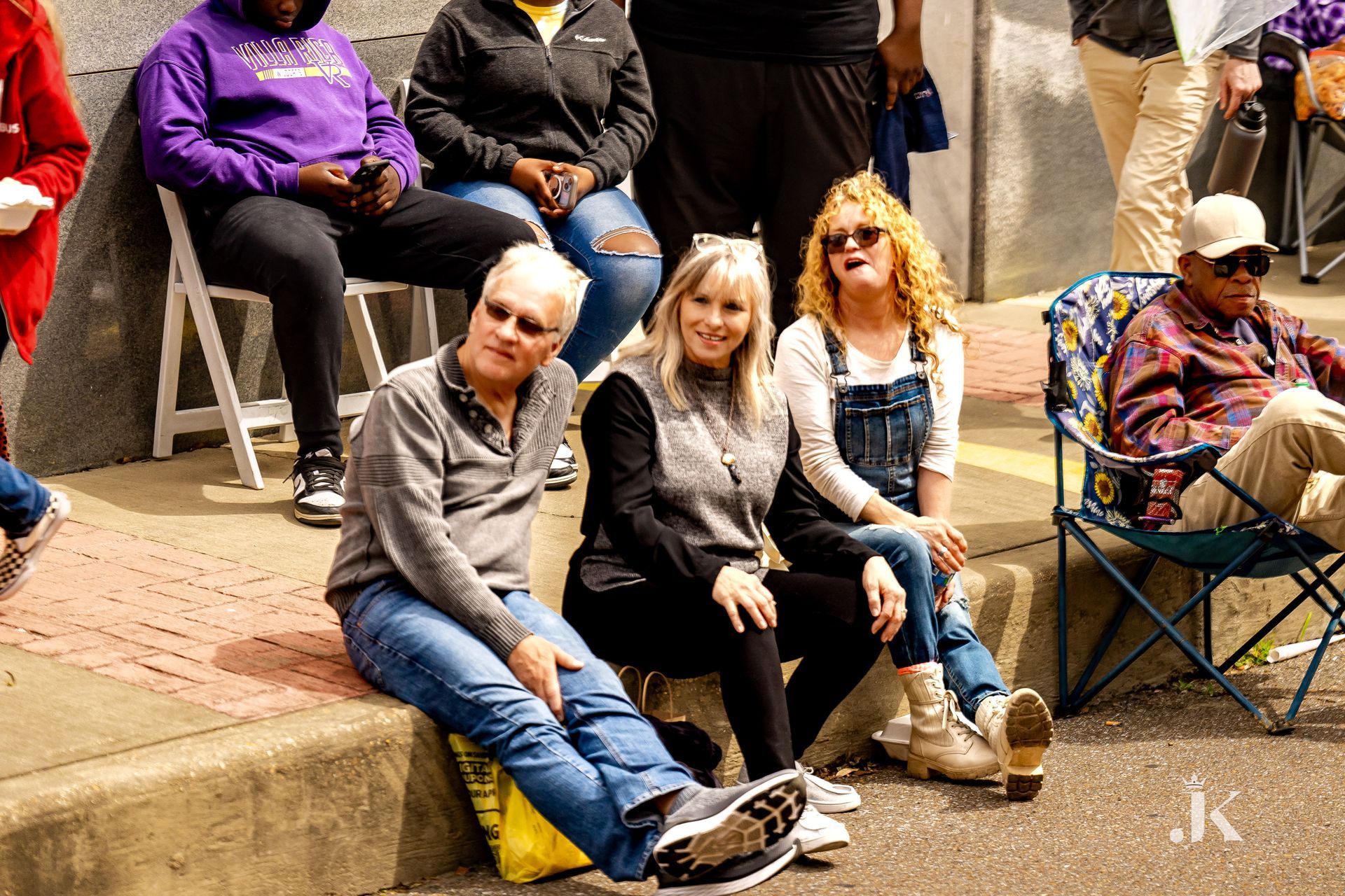A group of people are sitting on the sidewalk.