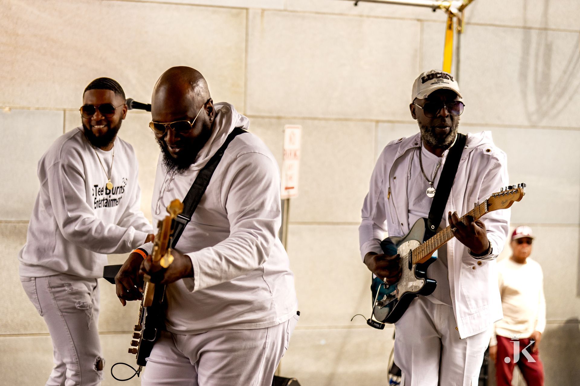 Three men in white shirts are playing guitars on a street.