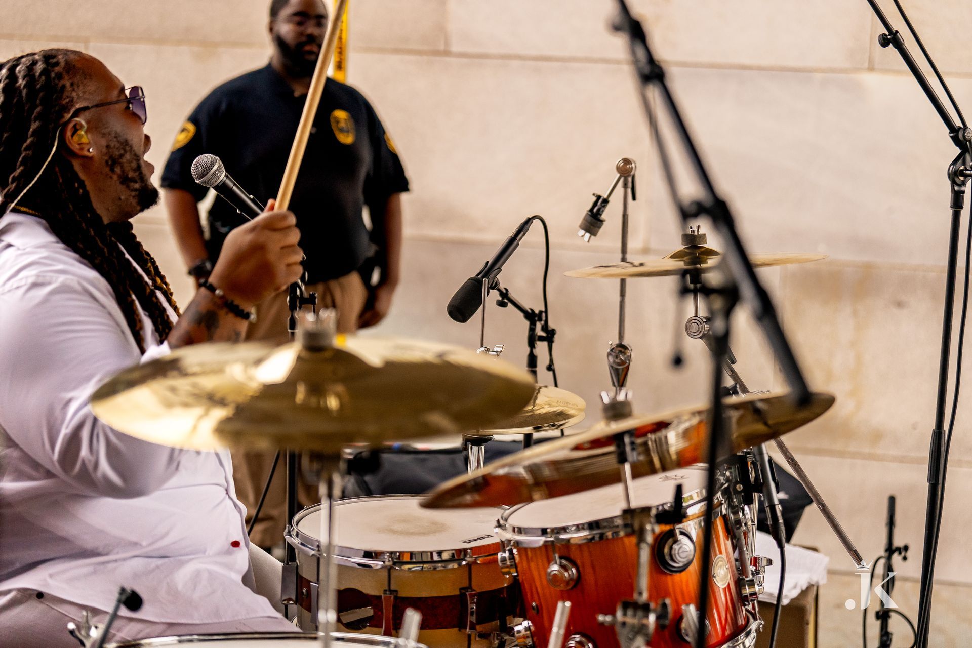 A man with dreadlocks is playing drums in front of a microphone.