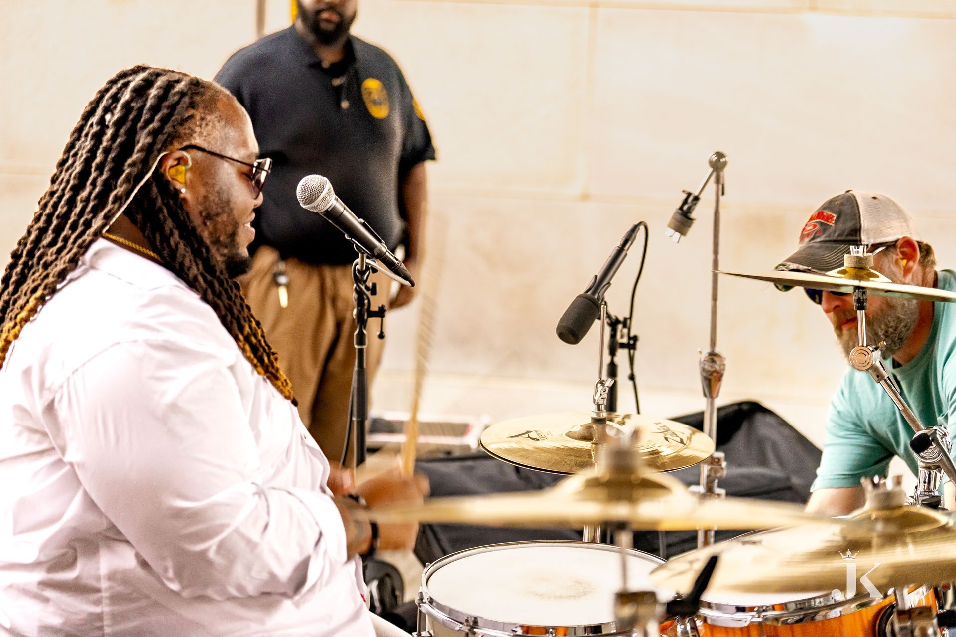 A man is playing drums while another man sings into a microphone.