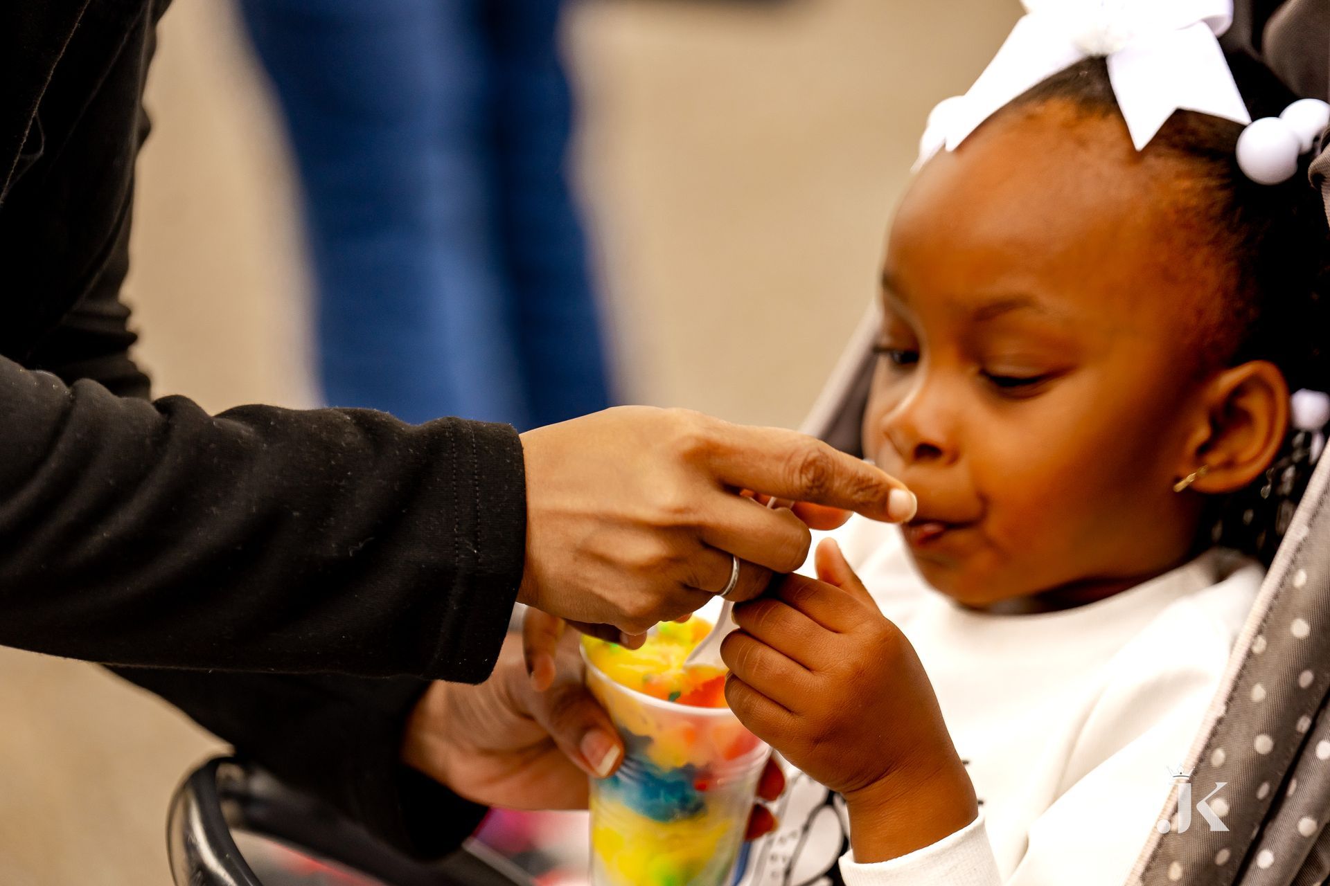 A little girl is eating ice cream from a cup while sitting in a stroller.