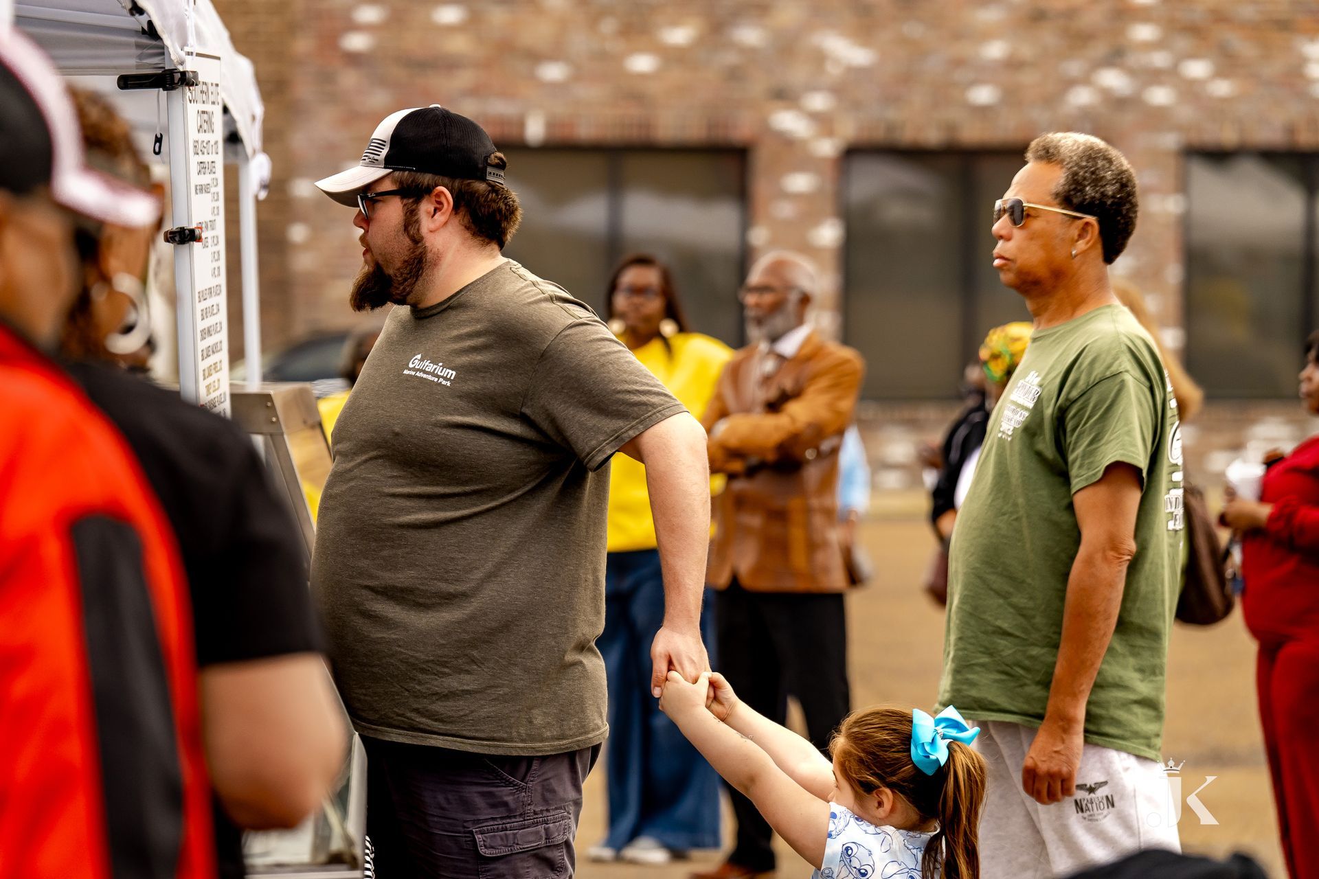 A man is holding a little girl 's hand while standing next to a group of people.