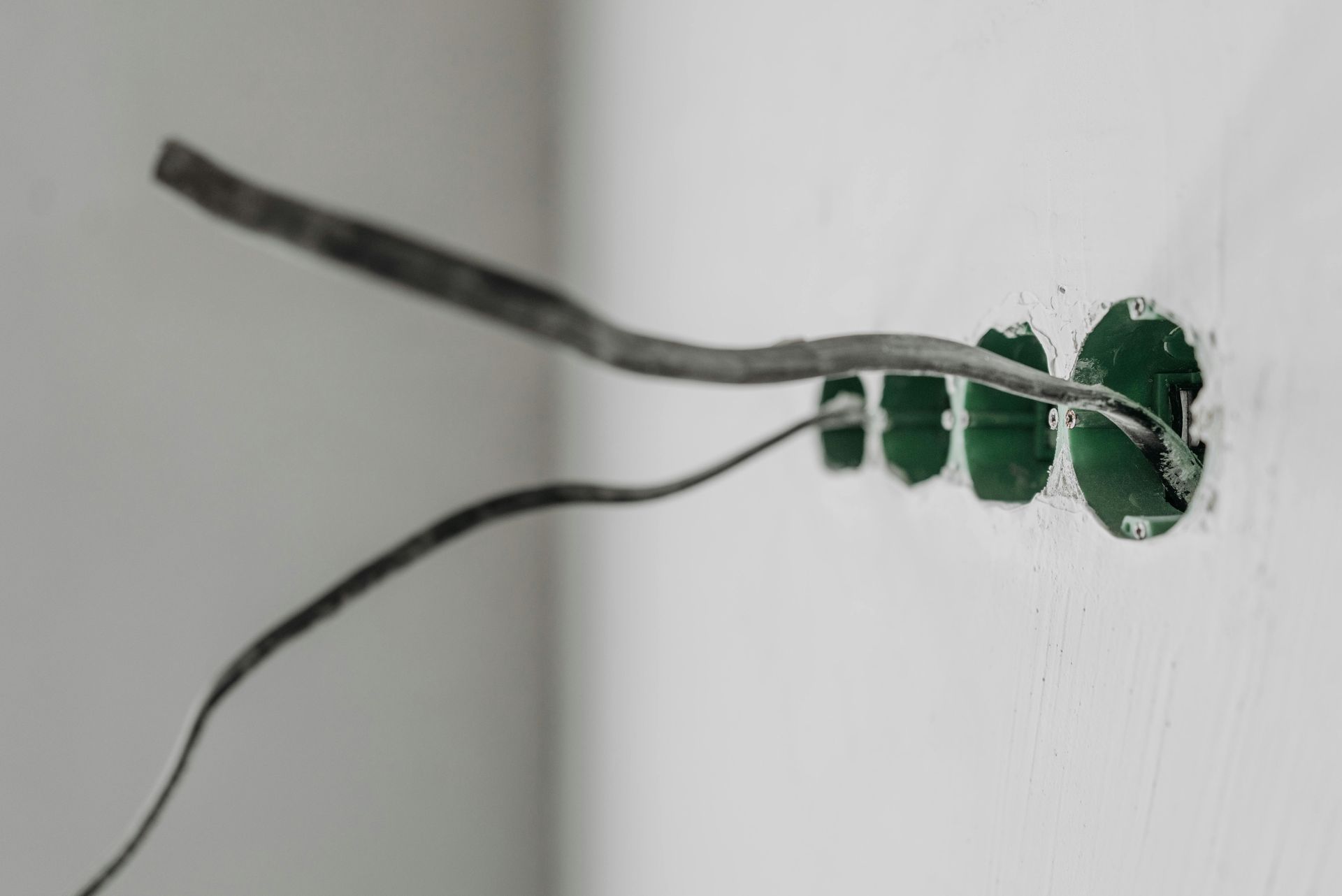 Exposed electrical wires extending from a green-ringed hole in a white wall.