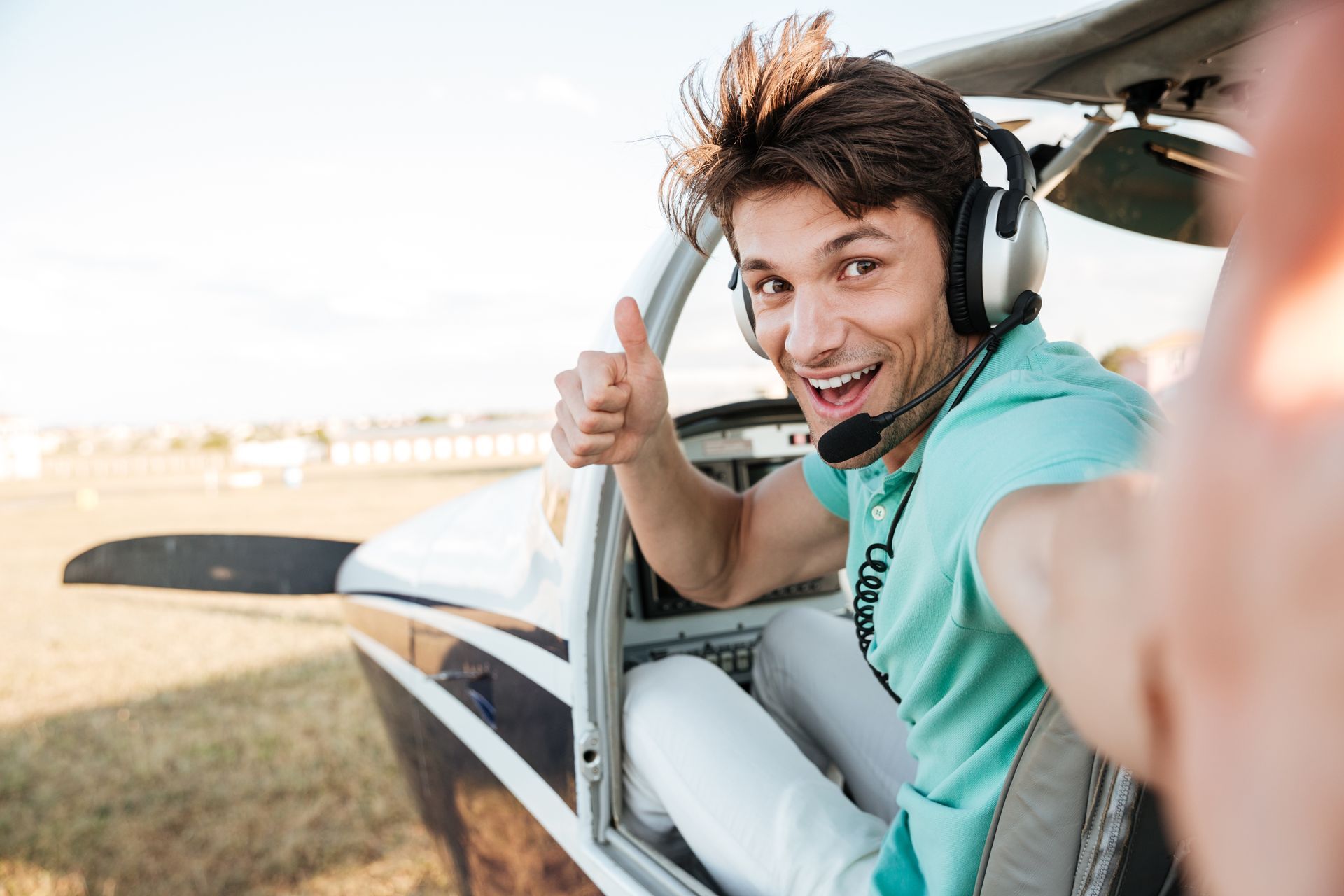 A man wearing headphones is sitting in a small plane and giving a thumbs up.