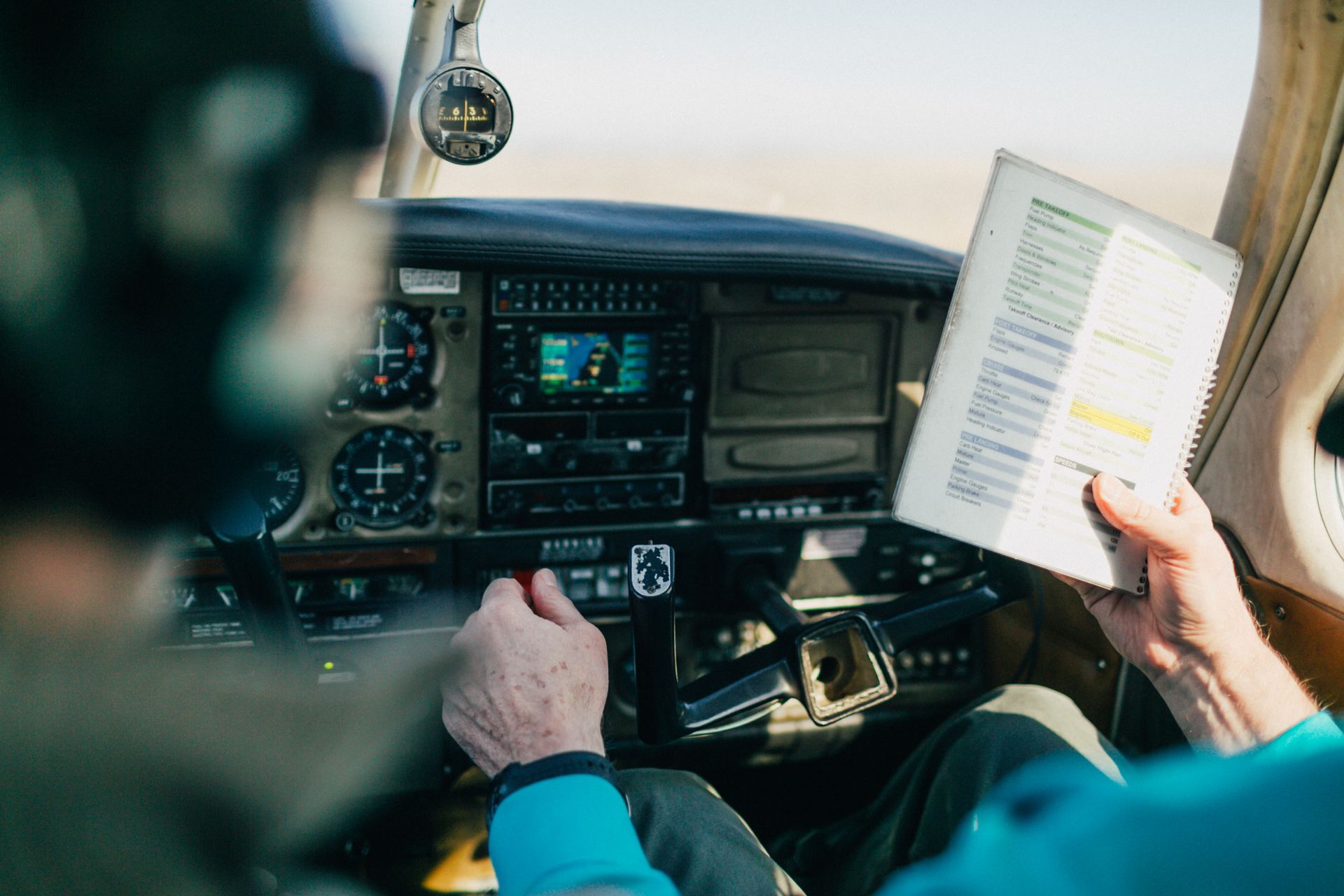 A man is sitting in the cockpit of an airplane reading a book.