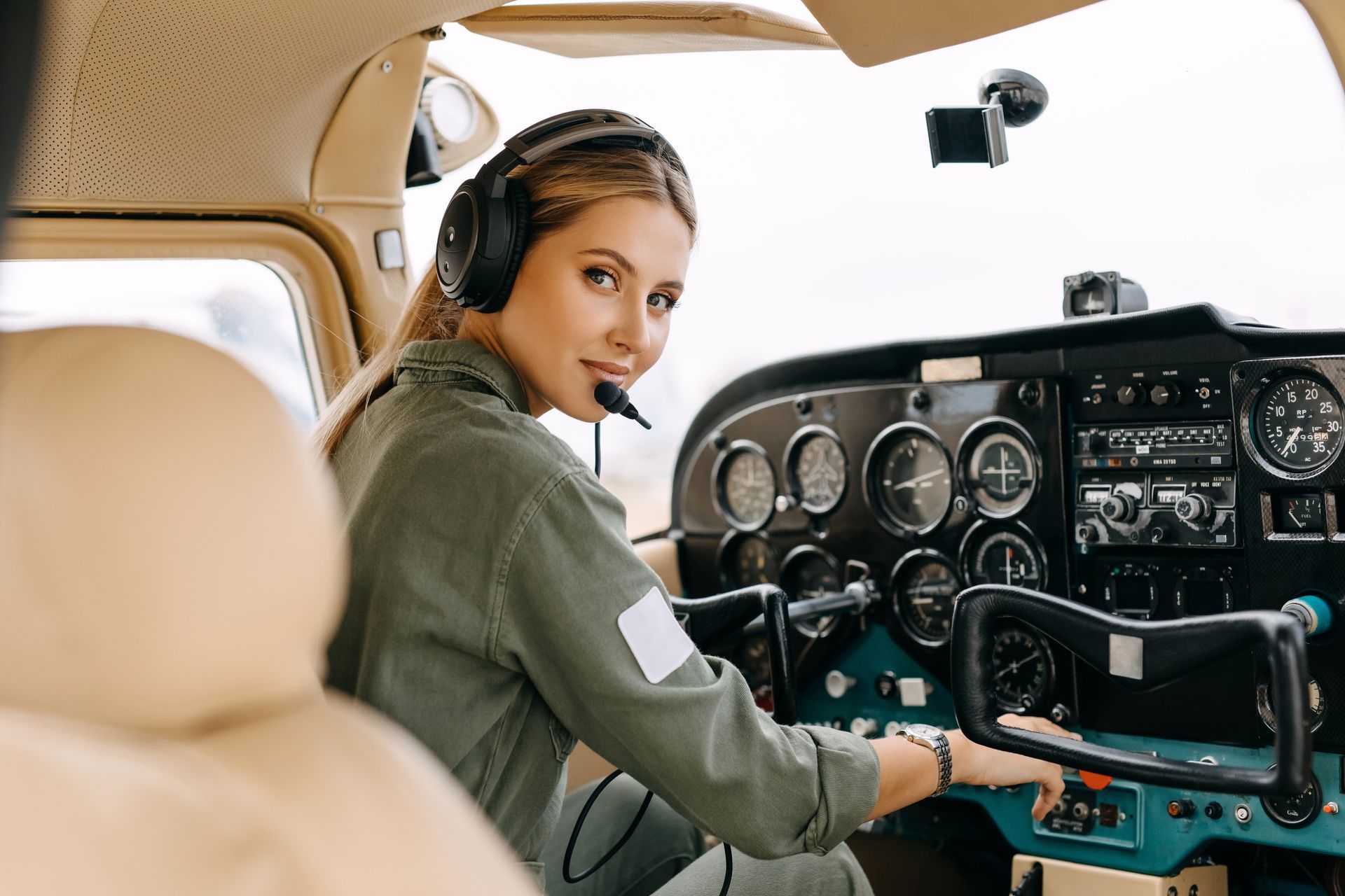 A woman is sitting in the cockpit of an airplane wearing headphones.