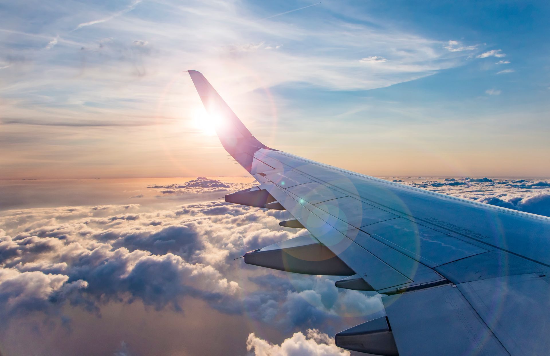 The wing of an airplane is flying through the clouds at sunset.