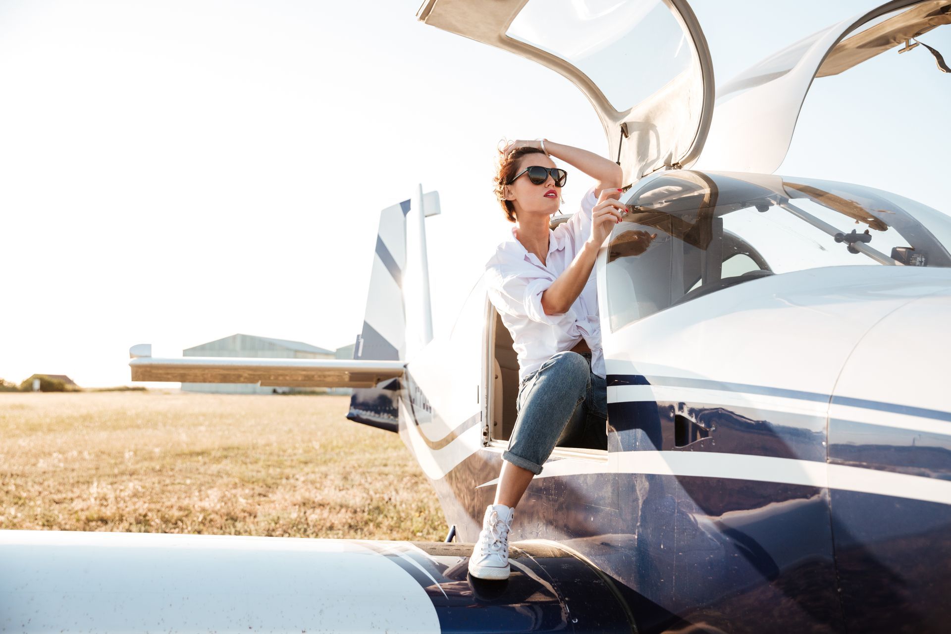 A woman is sitting on the wing of a small plane.