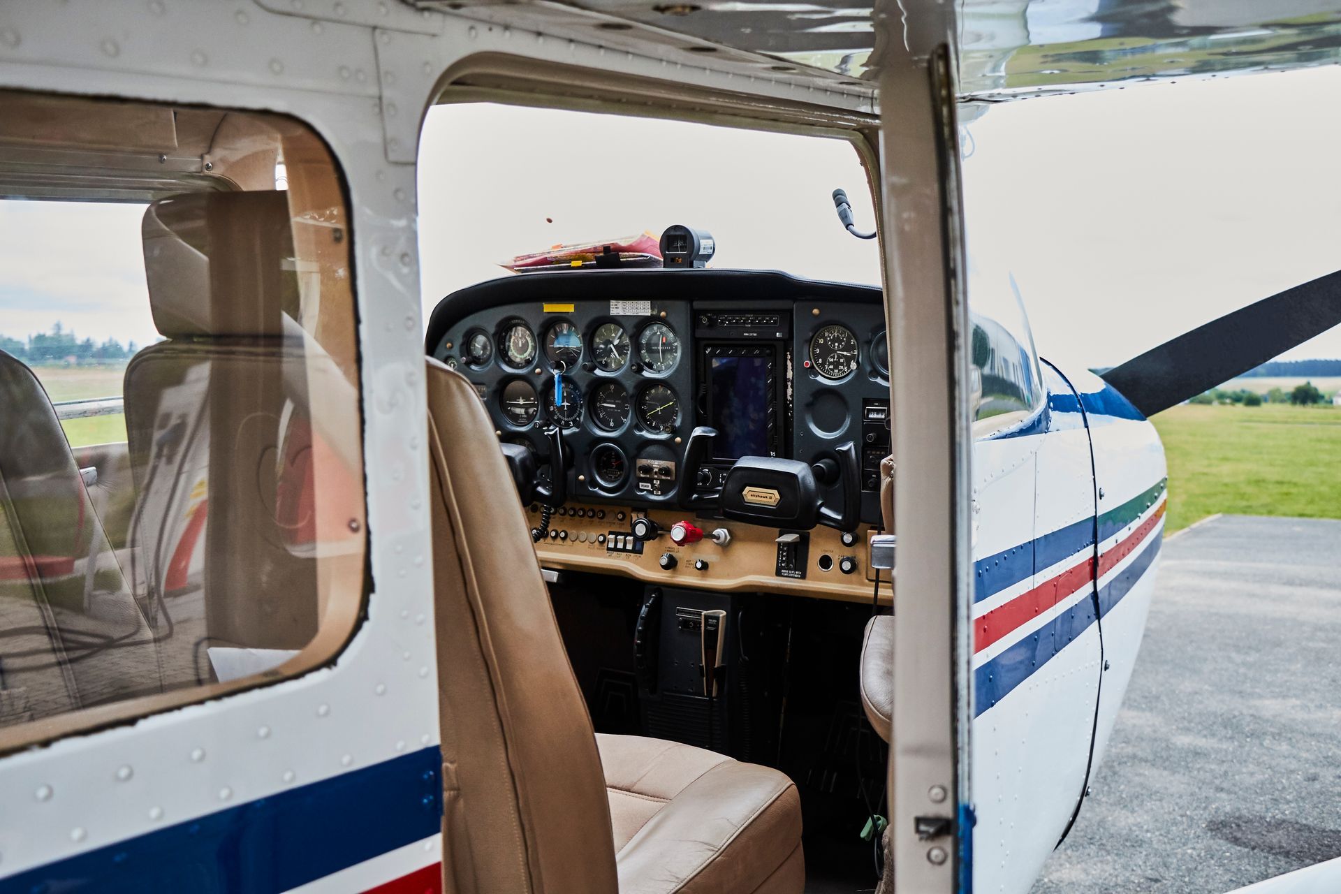 The cockpit of a small airplane is shown with the door open.