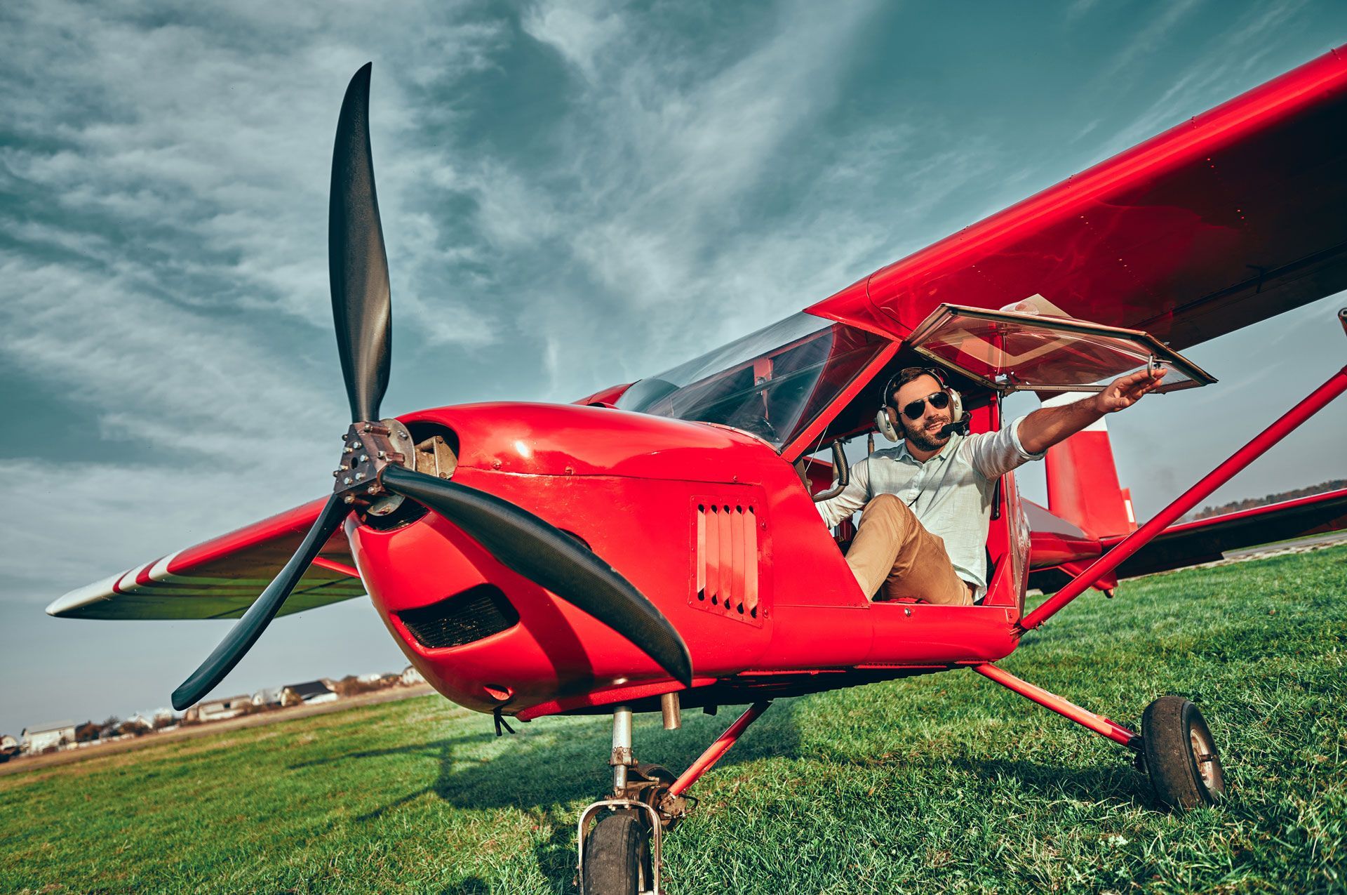 A man is sitting in a small red airplane on a grassy field.