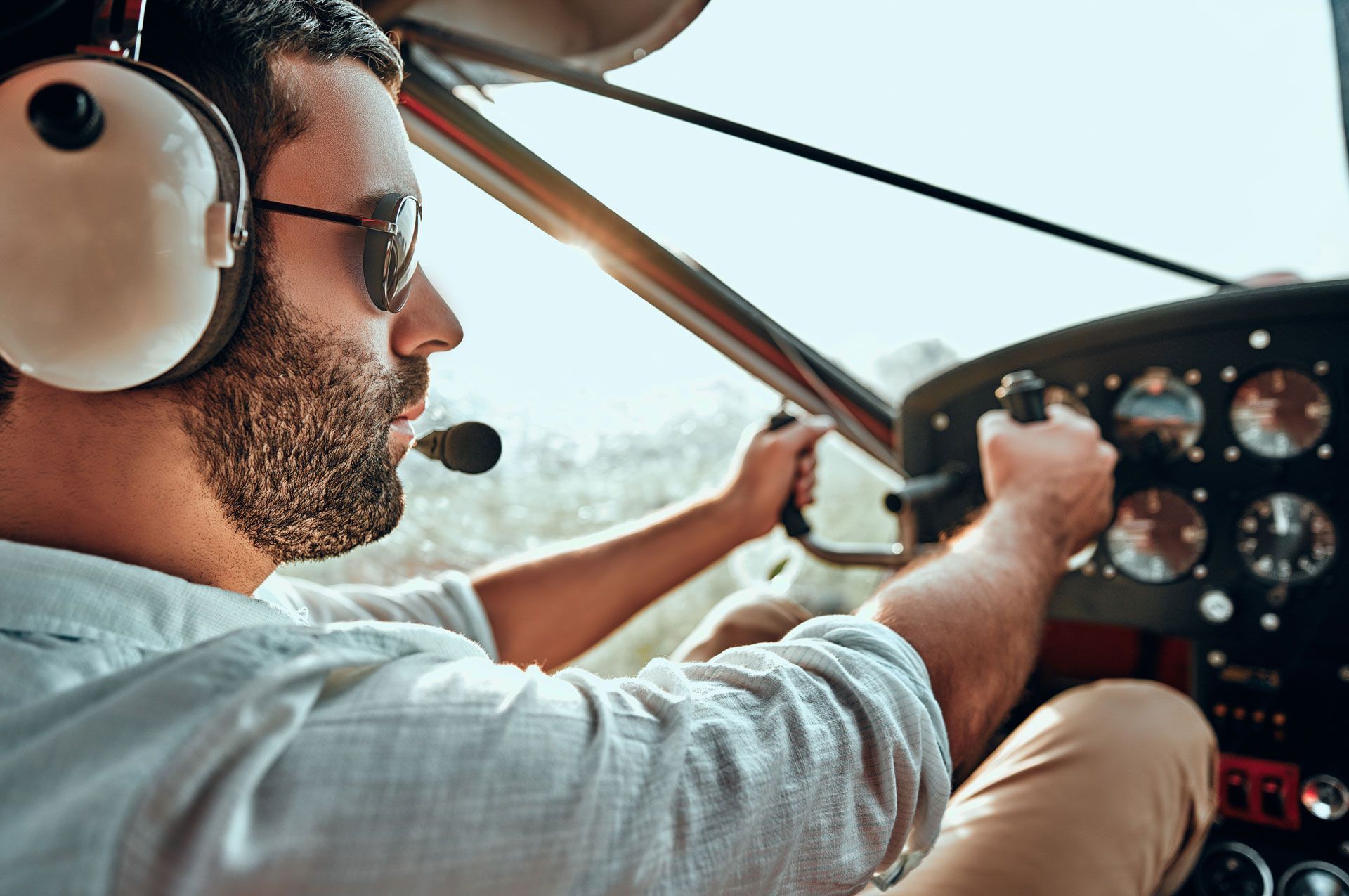 A man wearing headphones is driving a small plane.