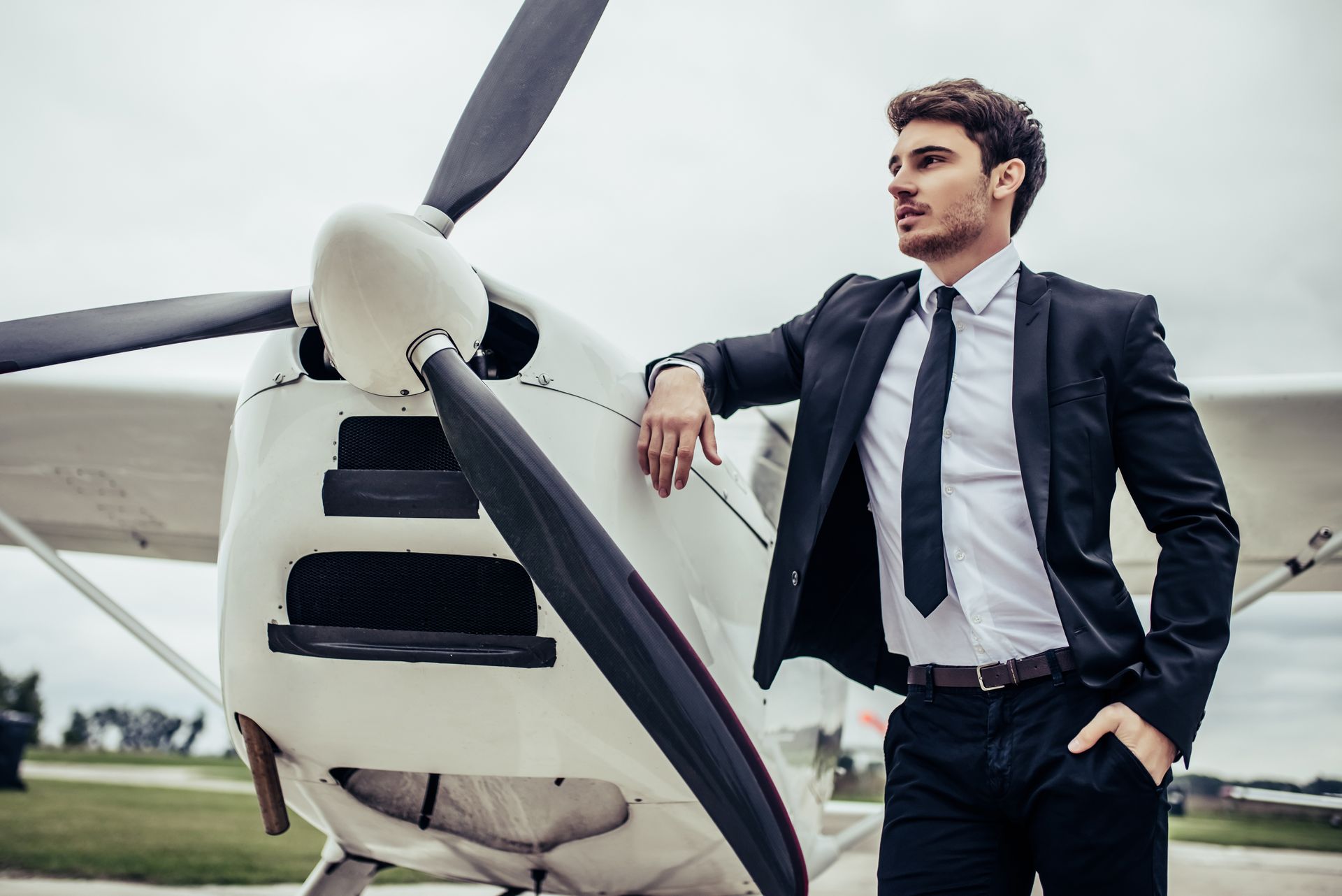 A man in a suit and tie is leaning against a small plane.