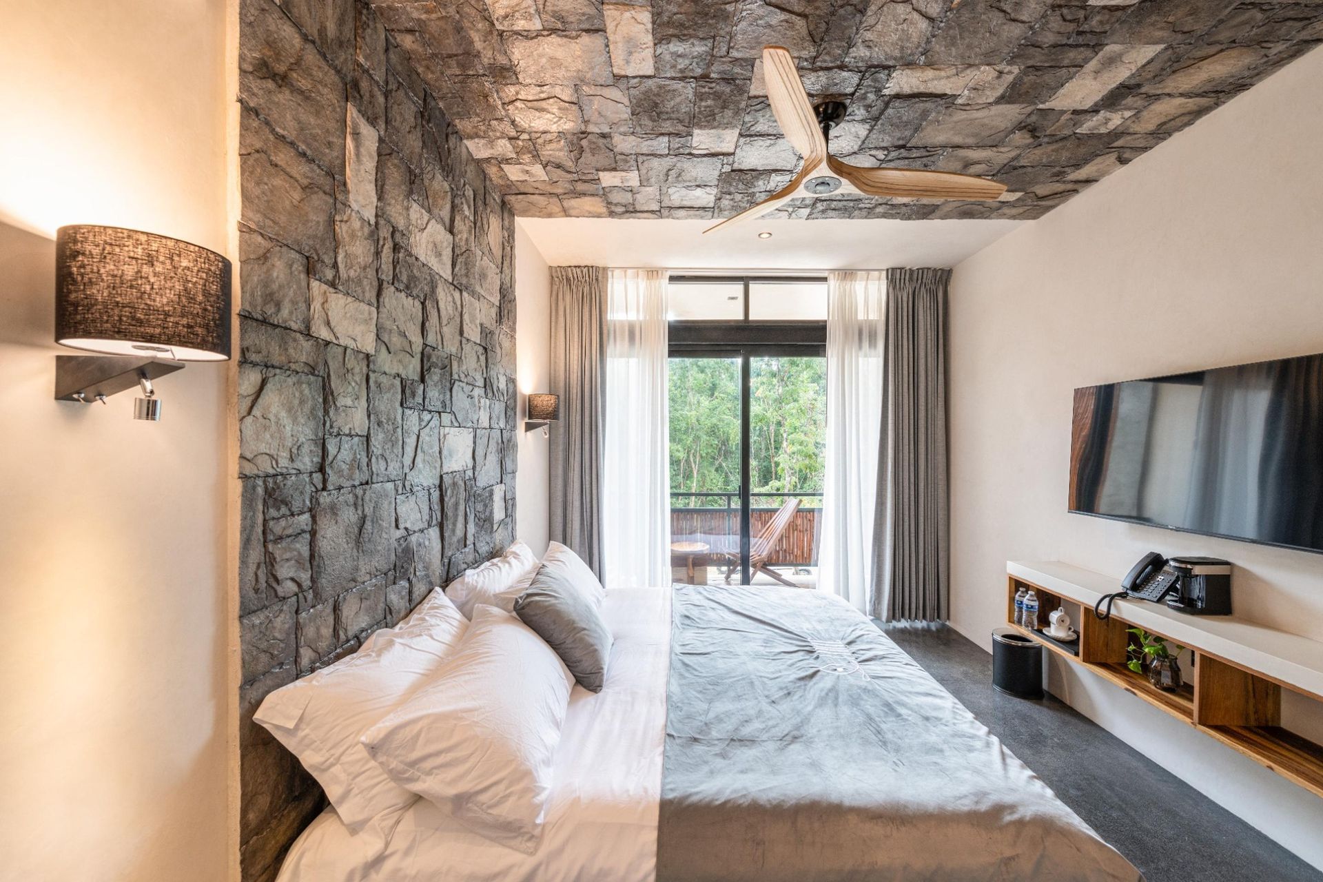 Bedroom with stone accent wall, ceiling fan, bed, TV, and balcony view.