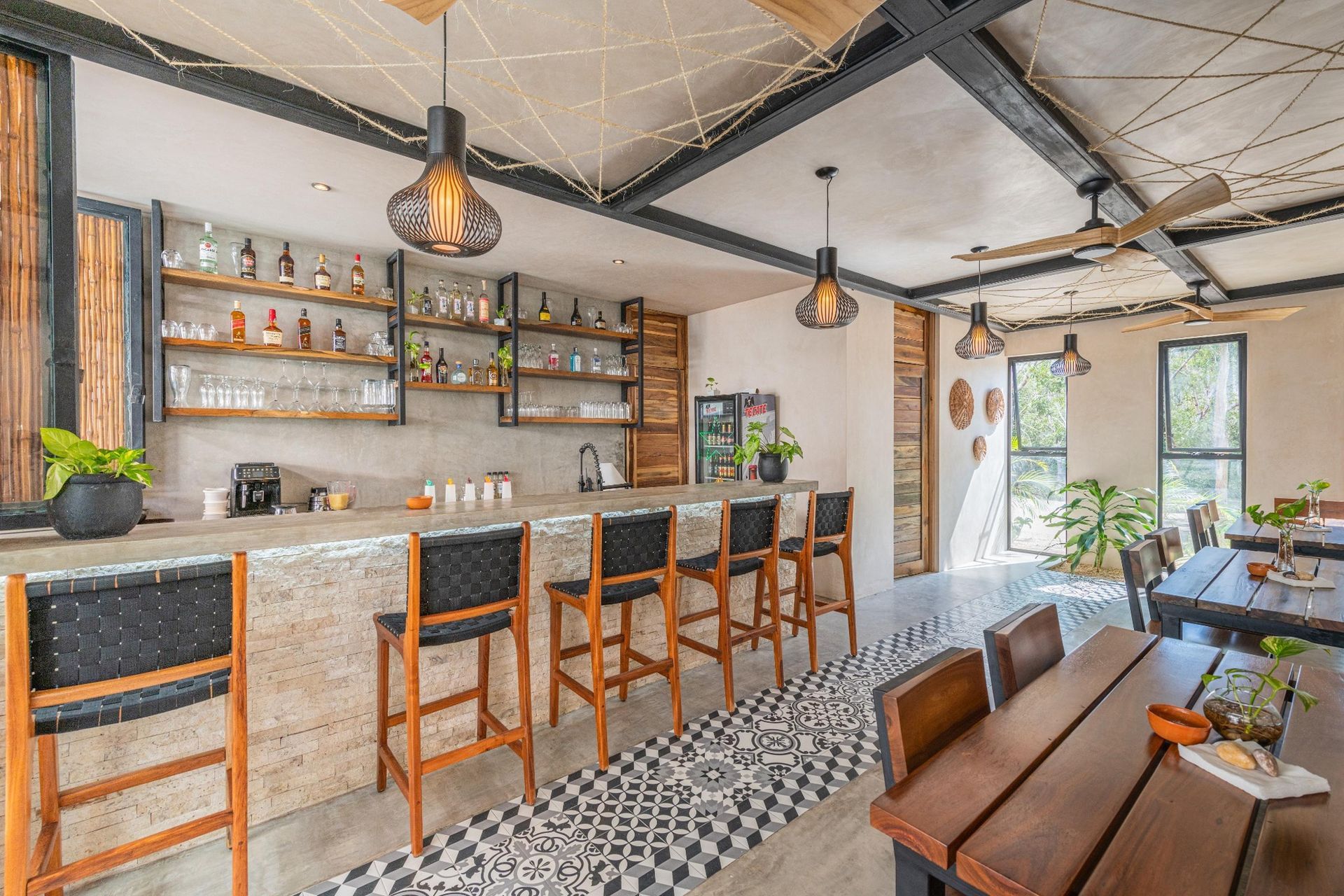 Bar and dining area with bar stools, wooden tables, shelves stocked with bottles, and decorative ceiling.